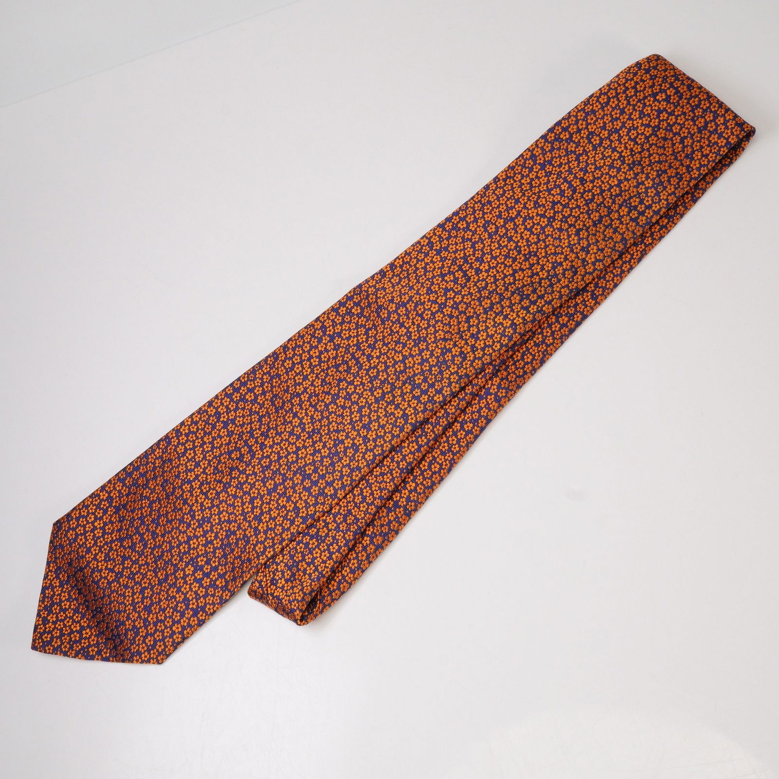 Versace Orange and Blue Floral Pattern Silk Tie: Versace silk tie featuring an allover floral pattern in vibrant orange against a deep blue background. The reverse bears the signature Medusa logo patch and woven Versace label. Made in Italy from pur