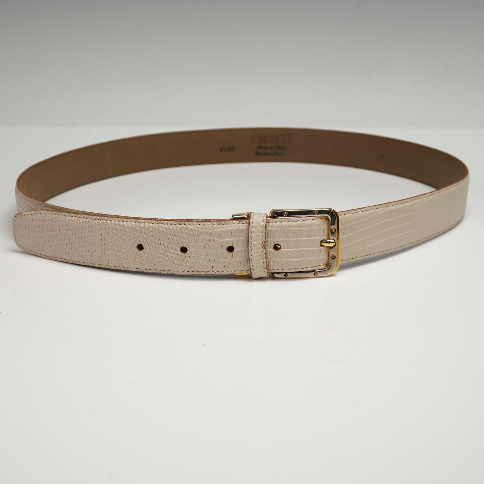 OGGI Italian Leather Embossed Belt: Leather belt featuring an elegant cream-toned embossed reptile pattern with a polished gold-tone buckle and hardware. Stamped Made in Italy, numbered 8485 and Size 37 marked on inside. Dimensions: 42"