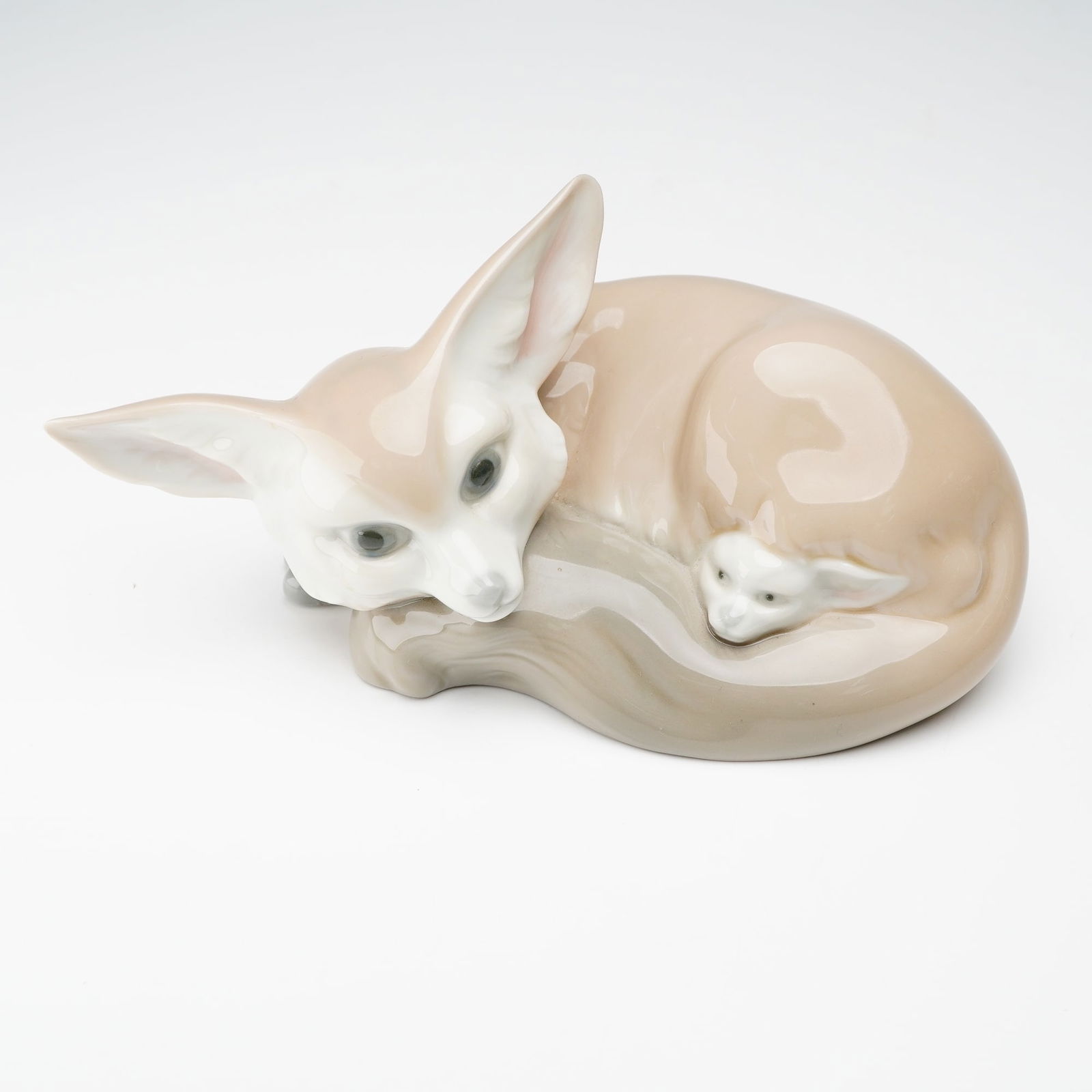 Lladro Porcelain Figurine, Fox And Cub 1001065: Figurine of a curled fox with a small cub nestled against its tail, finished in glossy neutral tones. Lladro backstamp on the underside. Artist: Fulgencio Garcia Issued: 1969-1985 Dimensions: 7"L x 3.