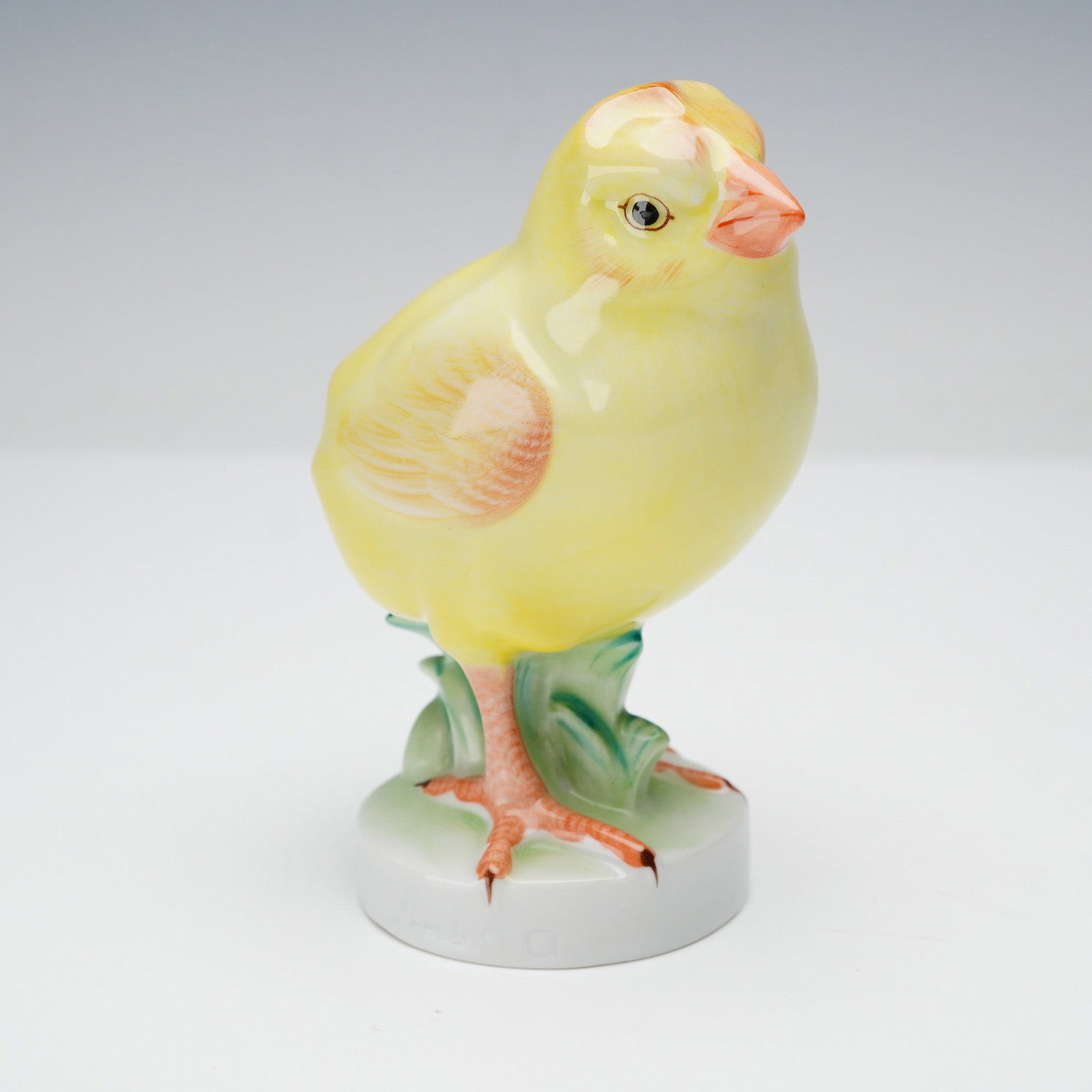Herend Porcelain Baby Bird Figurine, Chicken: This naturalistic figurine depicts a charming yellow chick rendered in soft blended tones, shown perched on a small green leaf base. Hand painted details add warmth to the feathering, wings, and facia