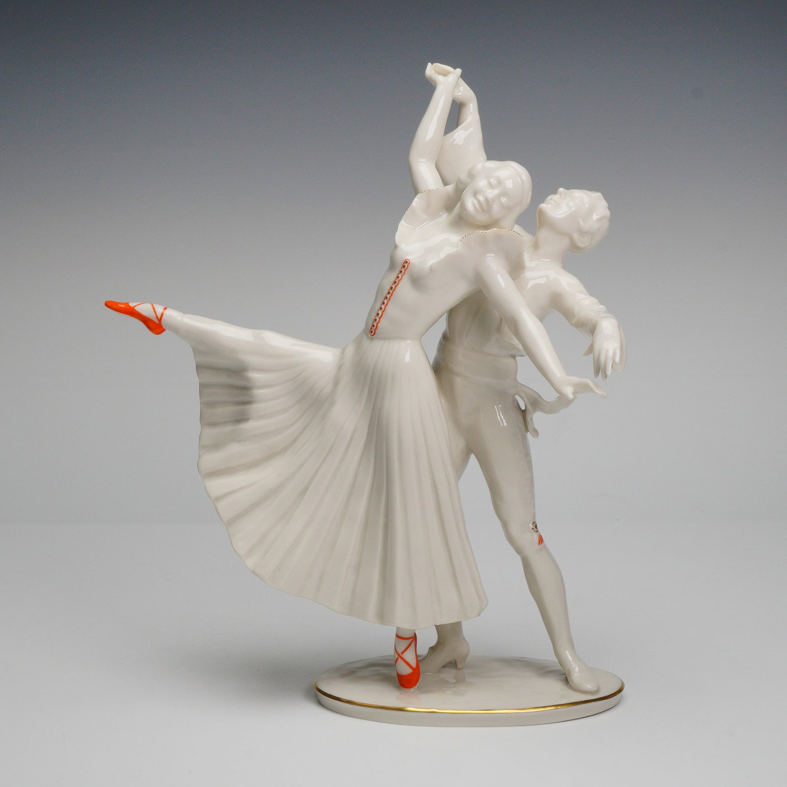 Hutschenreuther Ballet Dancers Porcelain Figurine: A fine Hutschenreuther Kunstabteilung porcelain figurine depicting a ballet duo in an elegant partnered pose, the female dancer extended en pointe with flowing pleated skirt and vivid orange ballet sl
