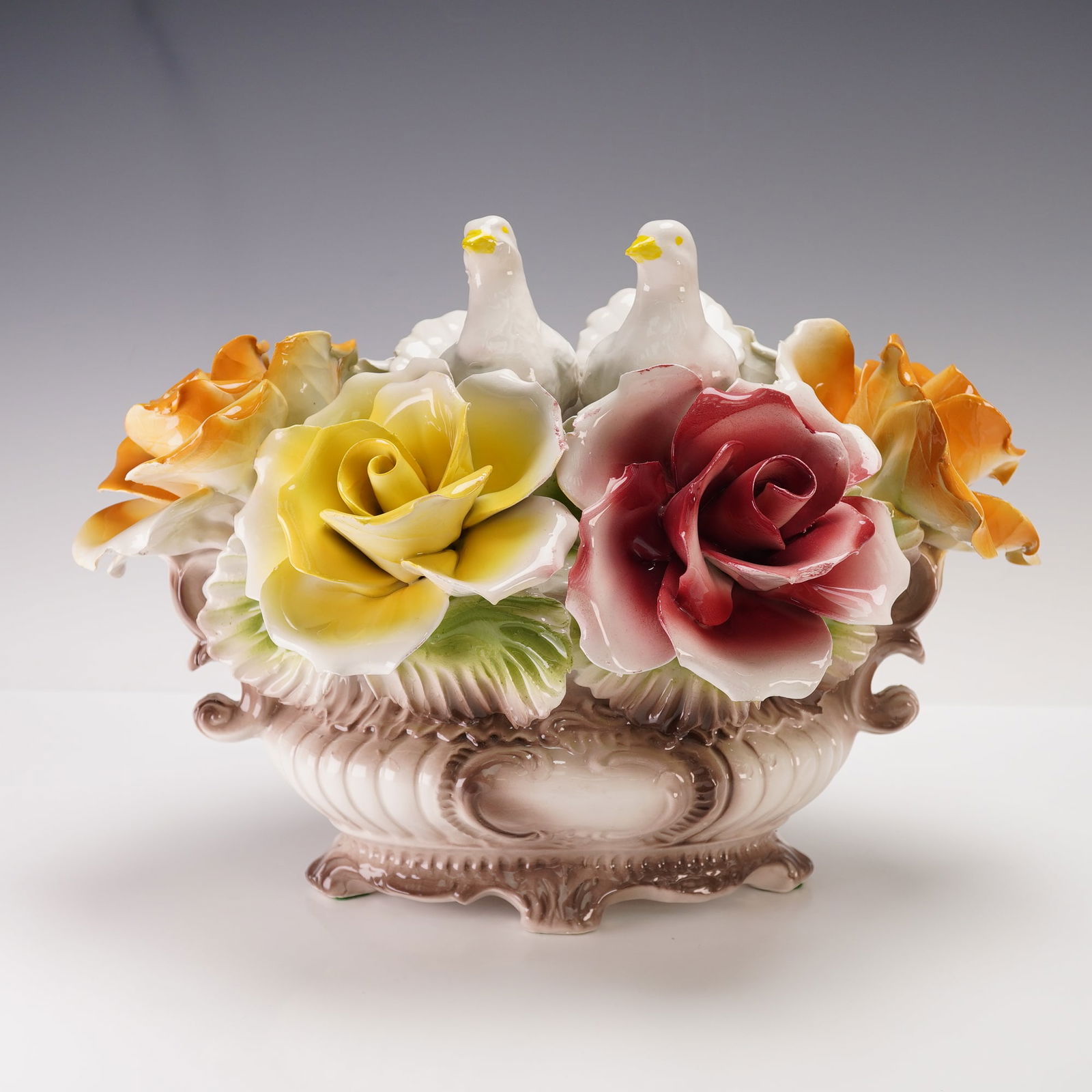 Capodimonte Figurine, Basket of Doves & Roses: Depicting a basket overflowing with hand-sculpted roses in vibrant hues of red, yellow, and orange, accompanied by two delicately modeled white doves perched at the center. The ornate vessel features