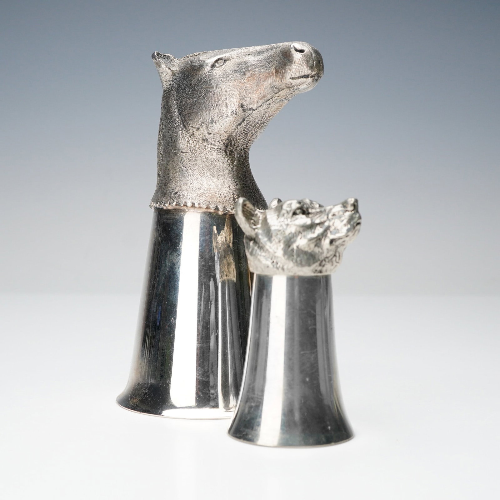 2pc Horse Head and Bear Head Metal Stirrup Cups: Two silvery-metal stirrup cups including one with a finely textured horse head and another with a detailed bear head showing deep fur texture and defined features. Dimensions: Largest item (Horse Cup)