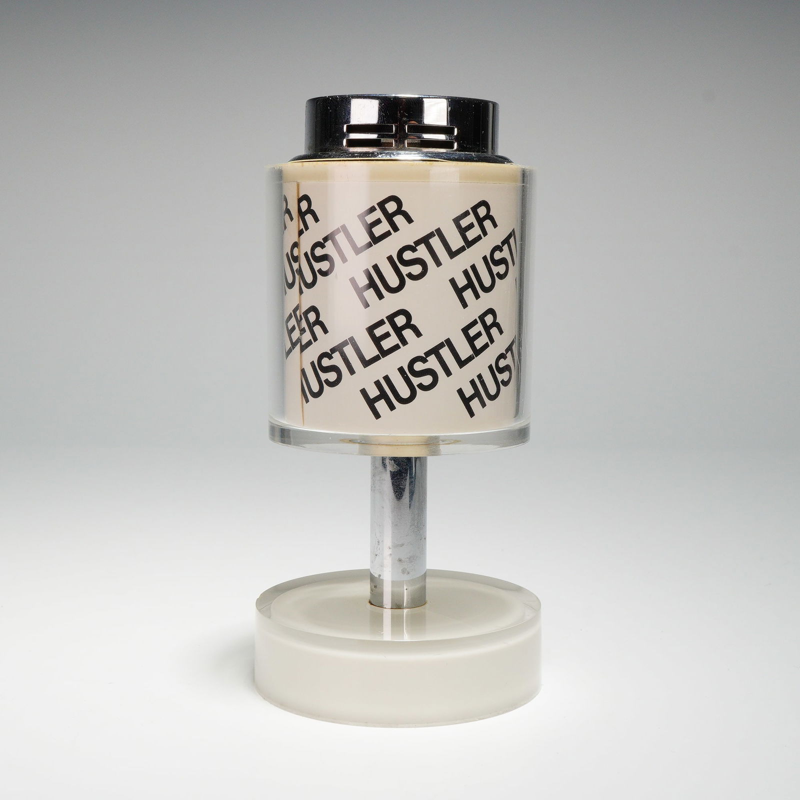 Scripto Hustler White and Chrome Lucite Table Lighter: This table lighter features a cylindrical Lucite body printed with the Hustler magazine pattern and a printed inscription reading Best Wishes Larry Flynt, who was the publisher of Hustler magazine. Th