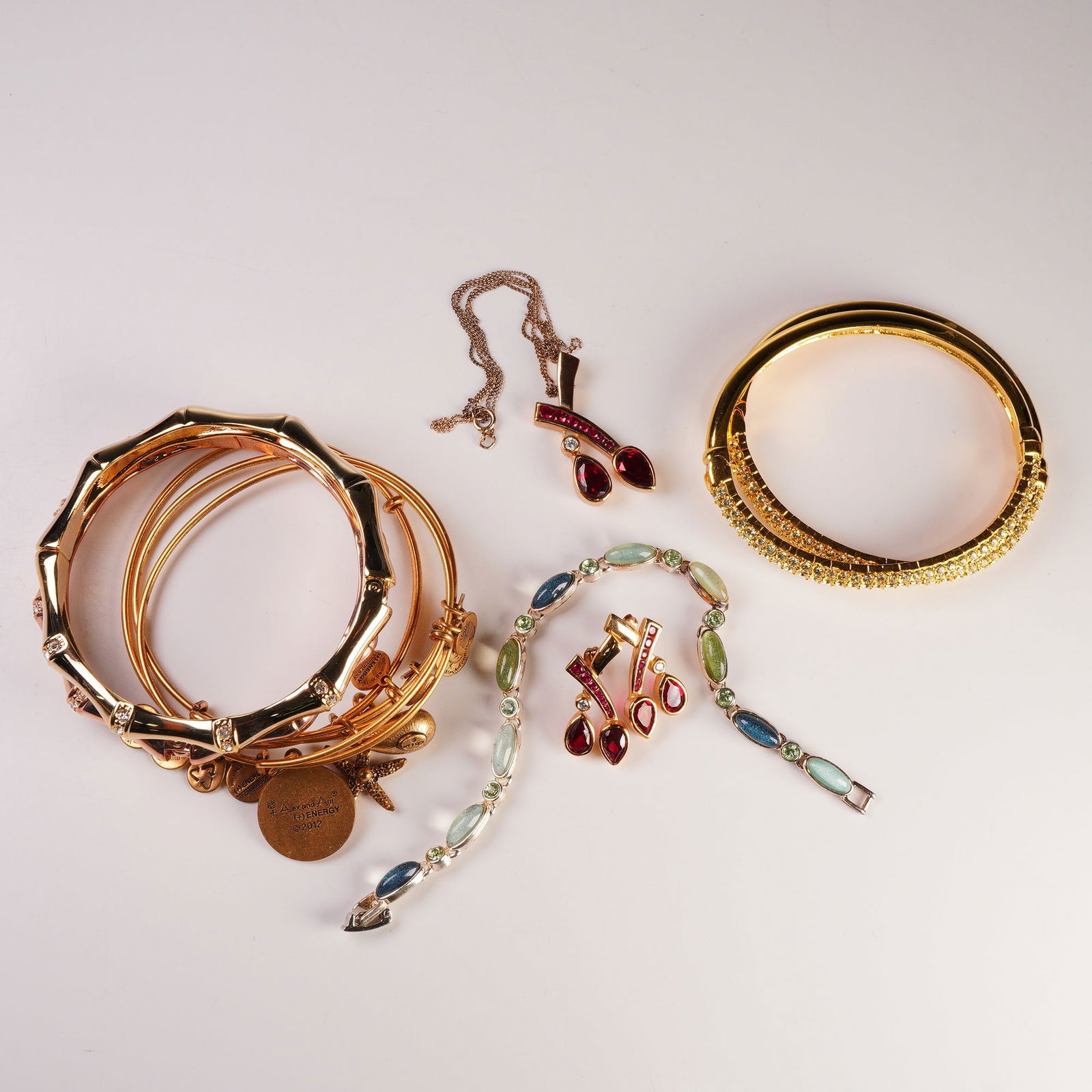 10pc Collection of Fashion and Designer Jewelry: Assorted ten-piece jewelry collection featuring a diverse mix of fashion and designer pieces. The lot includes a gold-plated necklace and matching earrings set with garnet-colored stones, both marked