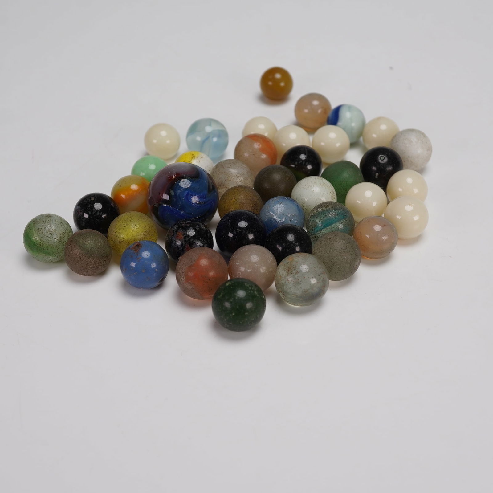 Collection of 38 Uranium and Mixed Glass Marbles: A colorful and varied lot of 38 vintage glass marbles featuring solids, swirls, and clear forms in a wide range of colors. The grouping includes a larger shooter marble alongside smaller examples, man