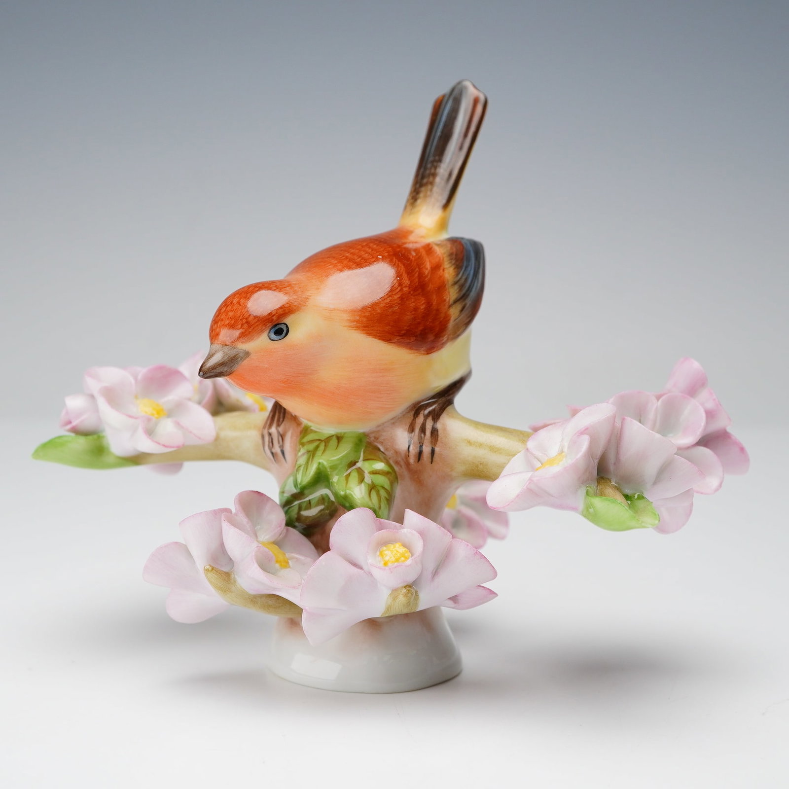 Herend Porcelain Figurine, Bird On Twig: Hand-painted naturalist colors, depicting a finch with orange and yellow plumage rests on a flowering branch, surrounded by finely shaped pink blossoms. Herend backstamp. Dimensions: 4.5"L x 3"W x 4"H