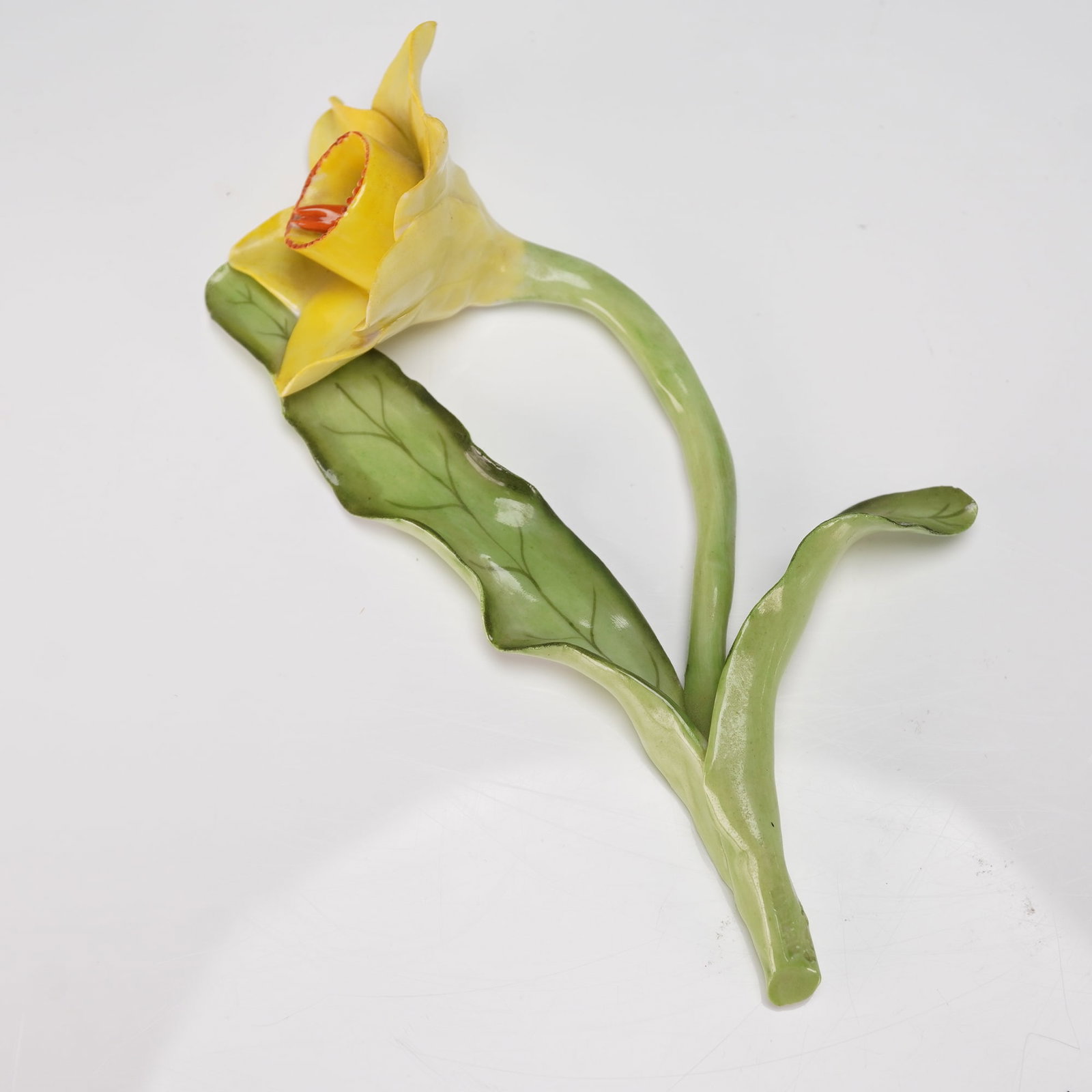 Herend Porcelain Figurine, Daffodil: A naturalistic yellow daffodil bloom rises from a long arched green stem with softly curved petals and delicate leaf accents, creating an elegant and expressive floral study. The underside bears the b