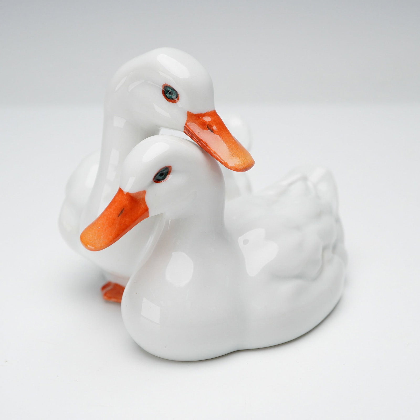 Herend Porcelain Figurine, Pair of Ducks: This figurine depicts two white Pekin ducks positioned closely together, each finished with bright orange bills and teal accented eyes. The bodies are shaped with subtle feather detailing and a glossy