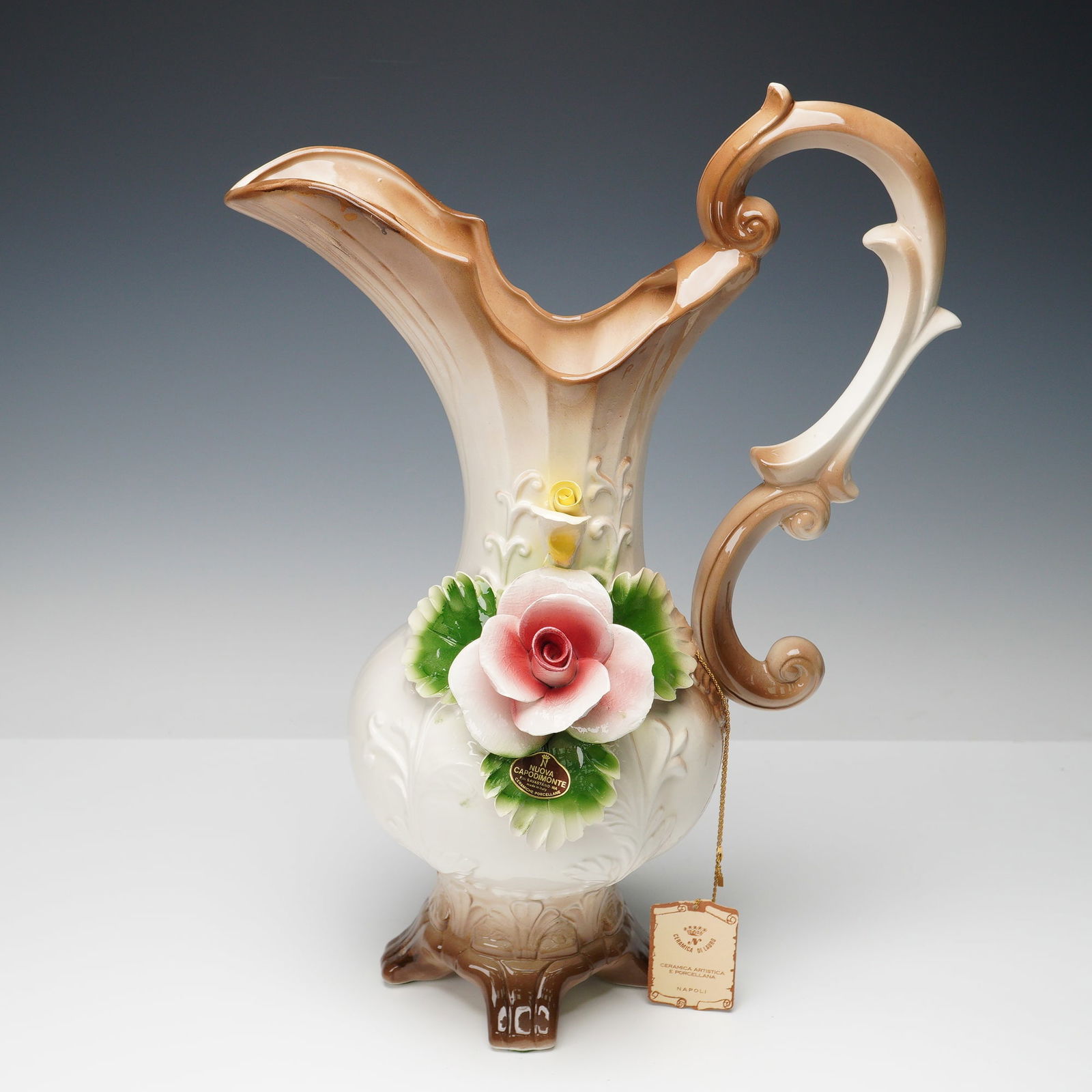 Nuova Capodimonte Large Pink Rose Pitcher: Nuova Capodimonte porcelain pitcher made in Italy, featuring a soft brown and cream glaze with raised scroll patterns. The piece is decorated with a large pink rose surrounded by green leaves and a sm