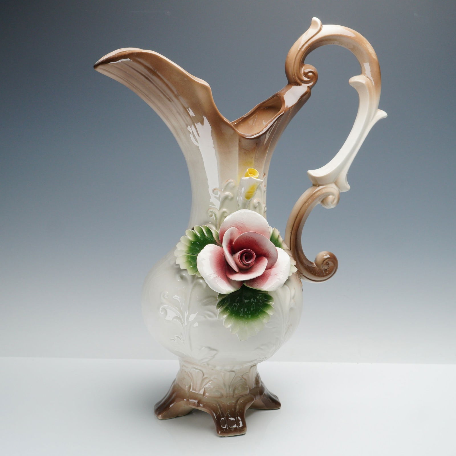 Capodimonte High Relief Floral Porcelain Pitcher: Capodimonte porcelain pitcher, hand-crafted in Italy with an ornate scrolled handle and raised foliate motifs. The body is highlighted by a finely modeled high relief applied rose in shades of pink wi