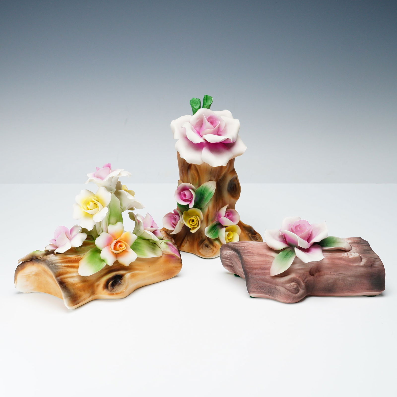3pc Nuova Capodimonte Porcelain Floral Sculptures: A three piece lot of Nuova Capodimonte porcelain floral sculptures, each hand-modeled and painted in Italy. The collection features blossoms in soft pastel shades of pink, yellow, and white arranged u