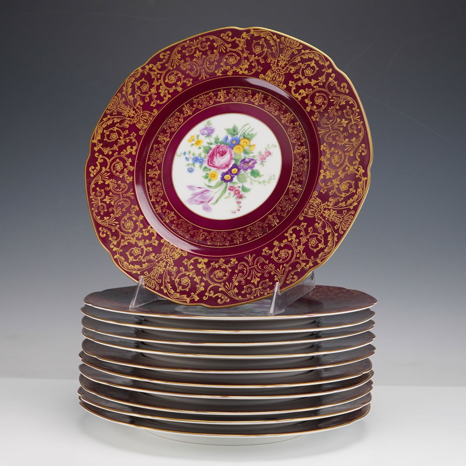 11pc Royal Bavarian Hutschenreuther Dinner Plates: This set includes eleven porcelain dinner plates made by Royal Bavarian Hutschenreuther. Each plate features a deep burgundy ground with an ornate gilt scroll border and a central roundel containing a