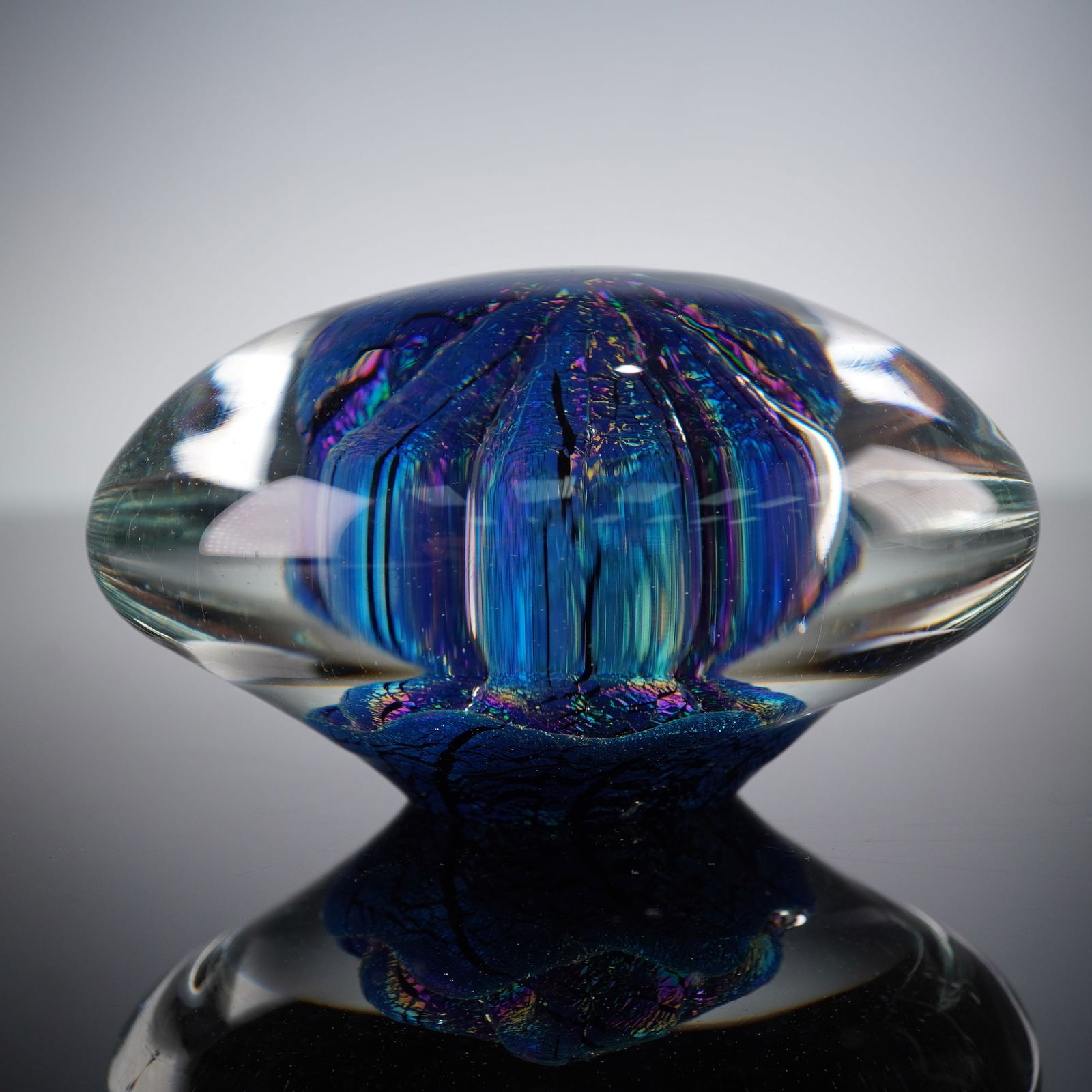 Eichholt Studio Art Glass Paperweight, 1998: A modern studio art glass paperweight by Eichholt, dated 1998. Crafted from clear glass, encapsulating a vibrant internal design featuring an abstract organic form in iridescent blues, purples, and gr