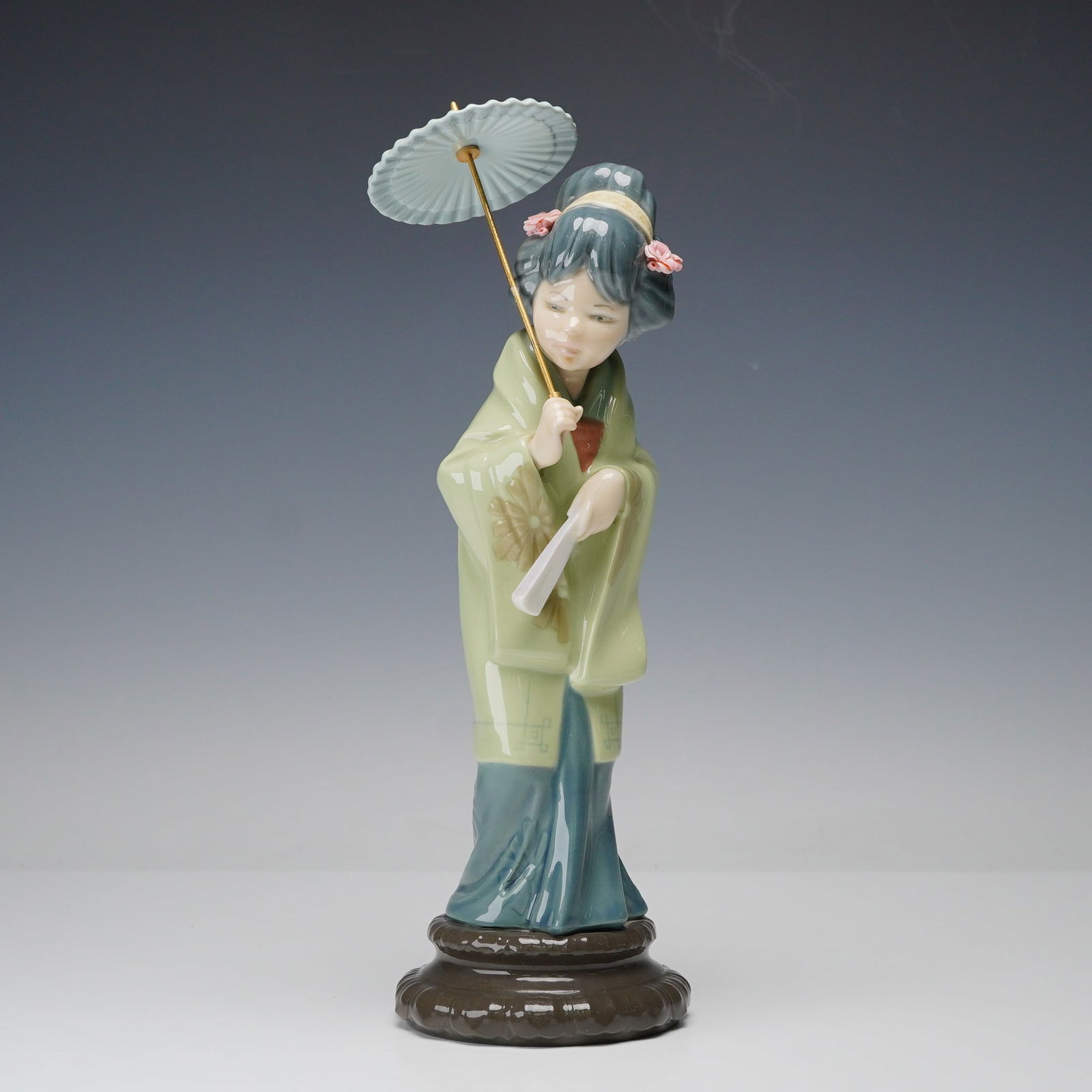 Lladro Porcelain Figurine, Oriental Spring 1004988: This figurine shows a woman holding a parasol above her shoulder while carrying a fan in her other hand. Her hair is arranged in a high style with applied porcelain flowers. She wears a long robe with
