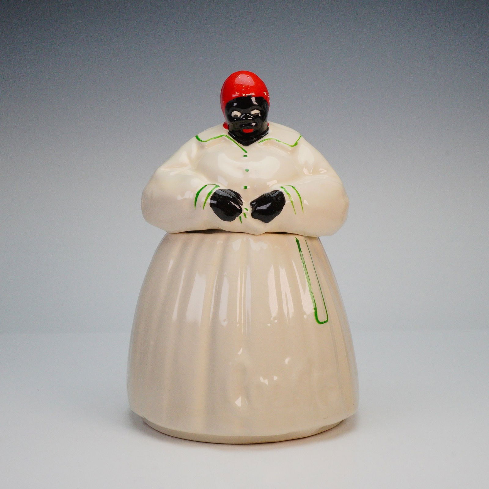 McCoy Black Americana Ceramic Cookie Jar w/ Lid: A midcentury McCoy ceramic Black Americana cookie jar modeled as a full-skirted woman, the removable upper body forming the lid, finished in a glossy cream glaze with hand-applied green trim and a viv