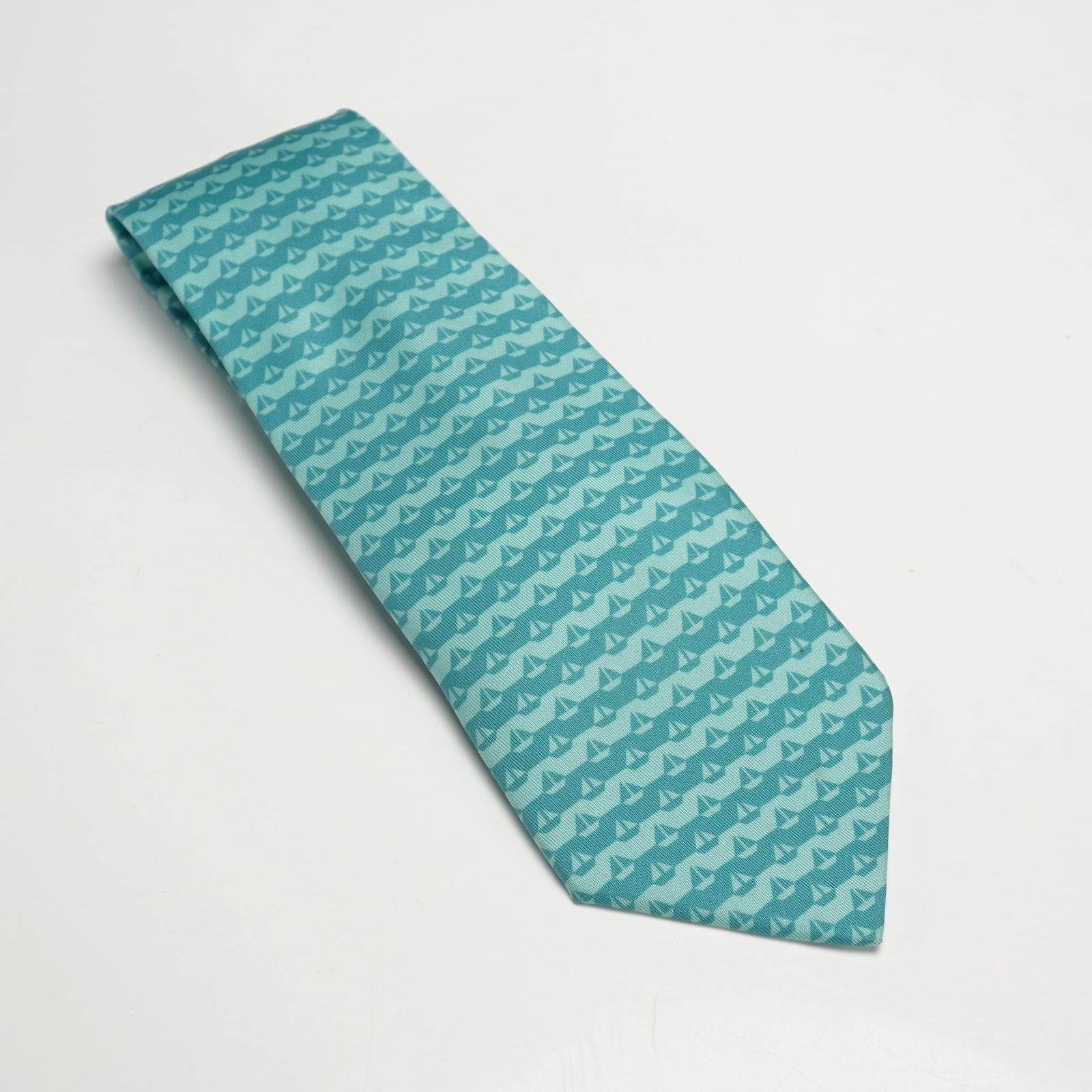 Hermes Paris Turquoise Sailboat Motif Silk Tie: A turquoise Hermes silk tie featuring sailboat motif woven in alternating shades of blue, crafted in 100 percent silk with the Hermes Paris logo and maker's label to the reverse. Dimensions: End to en