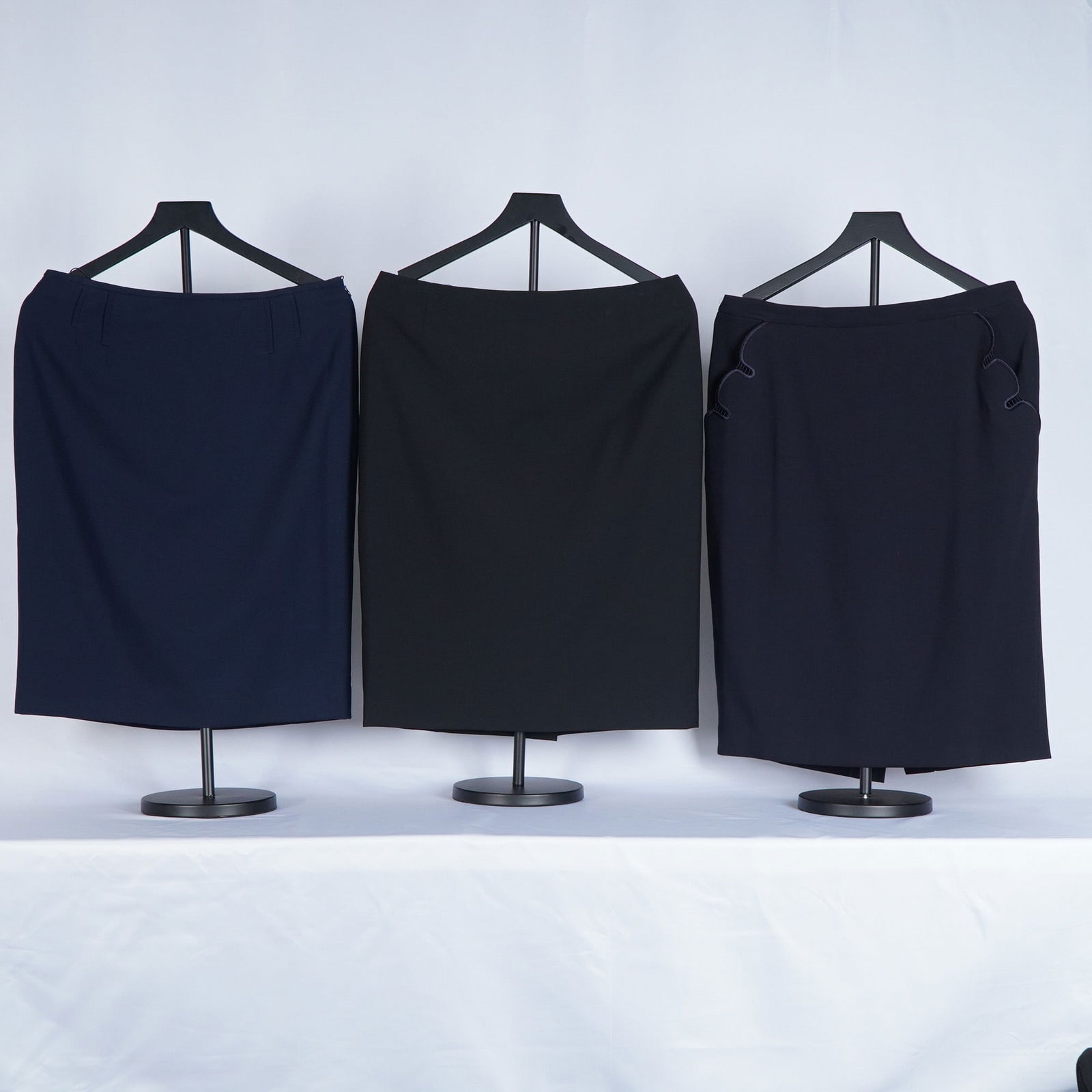 3pc Escada Straight Line Skirts: Straight line skirts, each tailored in classic minimalist silhouettes. This set includes a navy skirt, a black skirt, and a dark navy skirt featuring subtle wave-stitched accents at the hips. All piec
