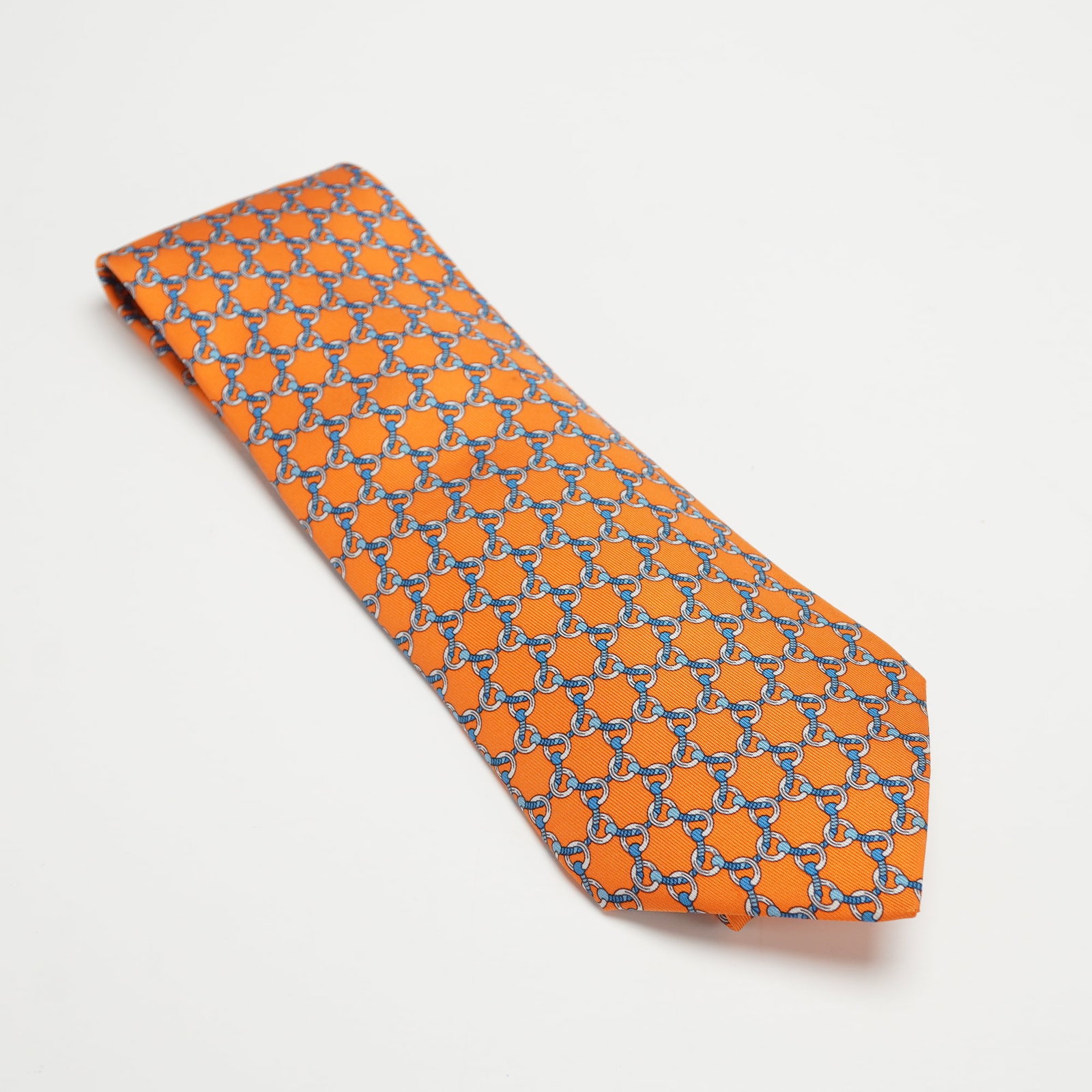 Hermes Paris Orange Chain Link Motif Silk Tie: Vibrant Hermes Paris 100 percent silk tie in bright orange, decorated with an allover interlocking chain motif in shades of blue and white, with woven Hermes Paris logo and horse and carriage labels t