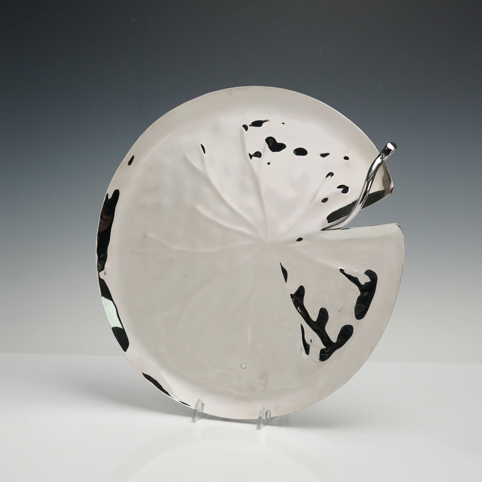 Michael Aram Stainless Steel Lily Platter: Sculptural stainless steel platter by Michael Aram, designed in the form of a stylized lily pad with raised stem detail. The surface features the organic textural variations and fluid contours charact