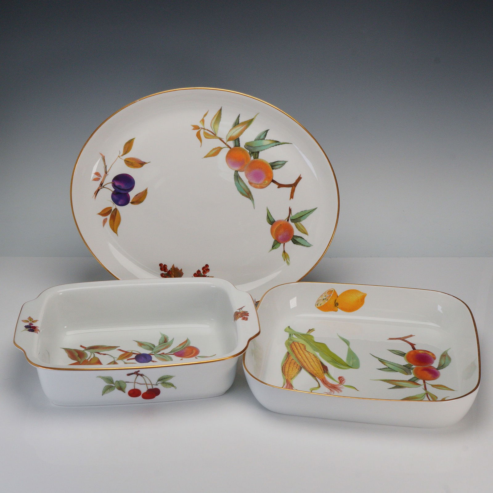 3pc Royal Worcester Porcelain Serveware, Evesham: A 3-piece group comprising one oval serving platter, one square baking dish, and one rectangular lasagna dish. Each piece decorated with assorted fruit motifs and gilt trim from the Evesham pattern. A