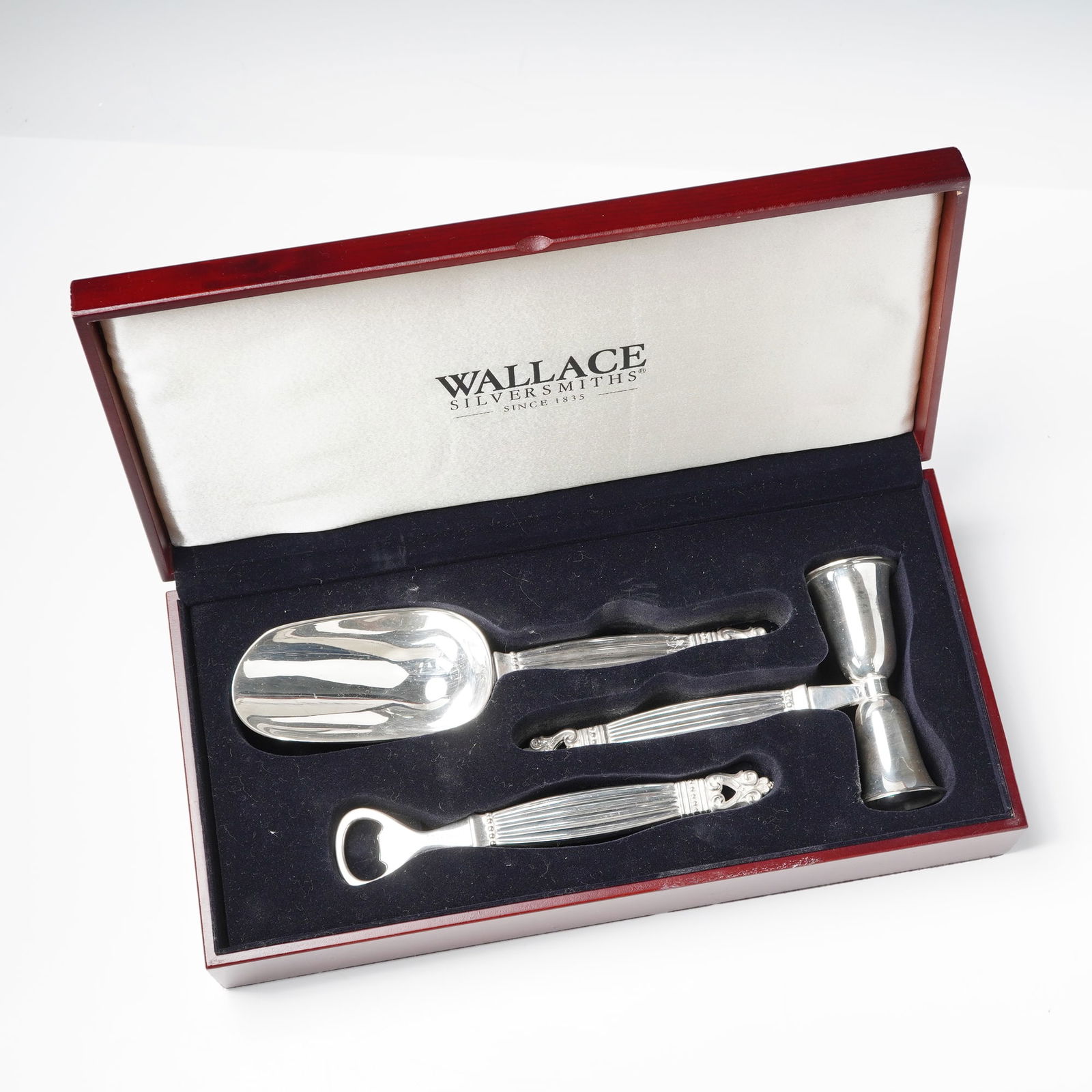 Wallace Silversmiths Silver Plated Barware Set: Set of three silver-plated bar tools by Wallace Silversmiths, including a bottle opener, double jigger, and ice scoop. Each piece features a ribbed handle with scroll finial design and Wallace hallmar