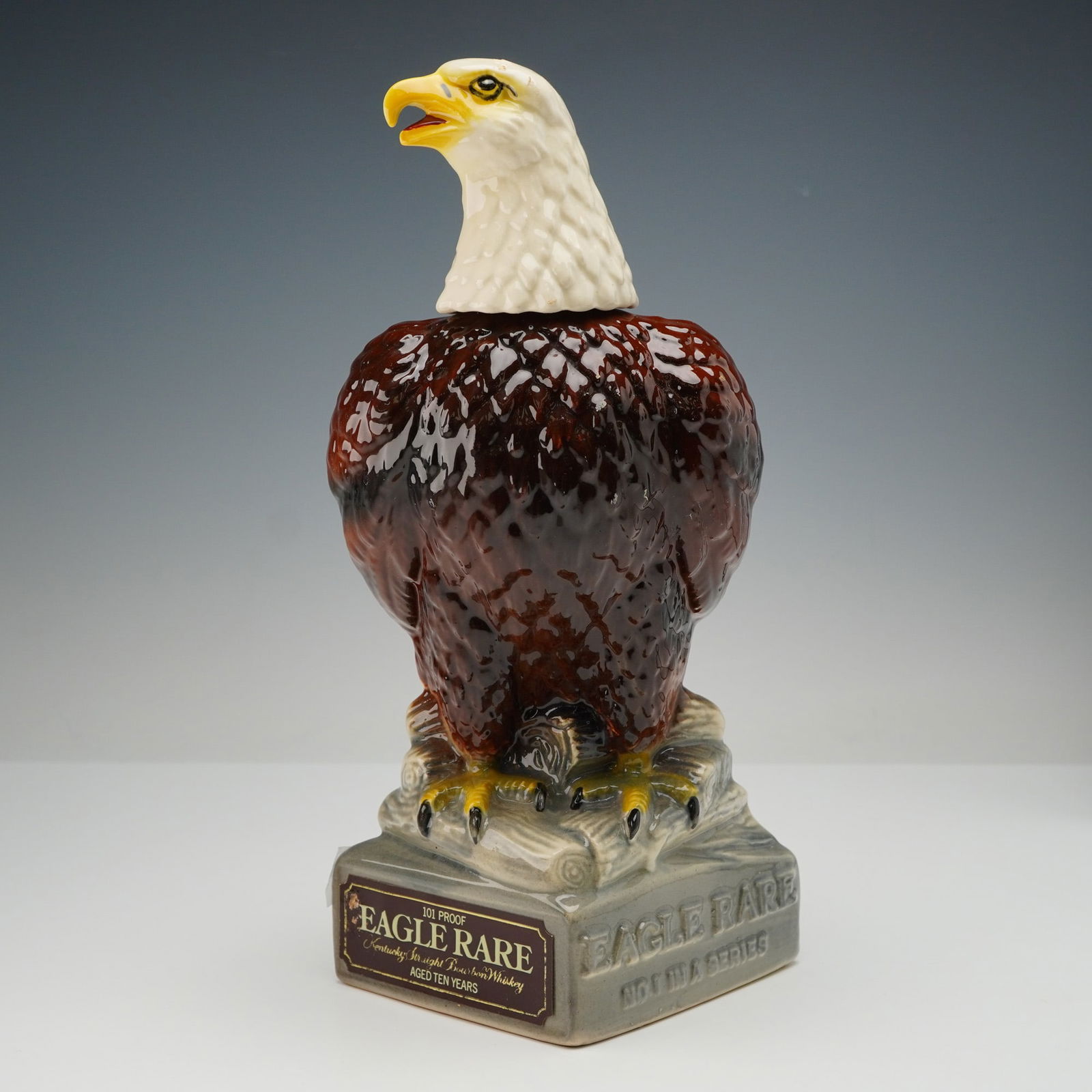 Eagle Rare 101 Proof Kentucky Straight Bourbon Whiskey Bald Eagle Decanter: A 1979 Eagle Rare 101 Proof Bald Eagle ceramic decanter, identified as No. 1 in a Series. This figural ceramic decanter is molded and glazed to depict a bald eagle standing on a textured, rock-like ba
