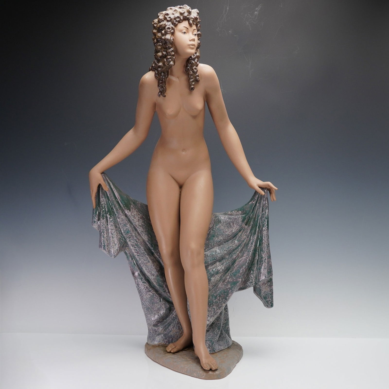Lladro Gres Porcelain Sculpture, Innocence 01013558.3: Innocence (Green), depicting a nude young woman with elaborately curled hair as she lifts the edges of a textured, green-mottled draped cloth behind her. Rendered in Lladro's signature matte Gres fini