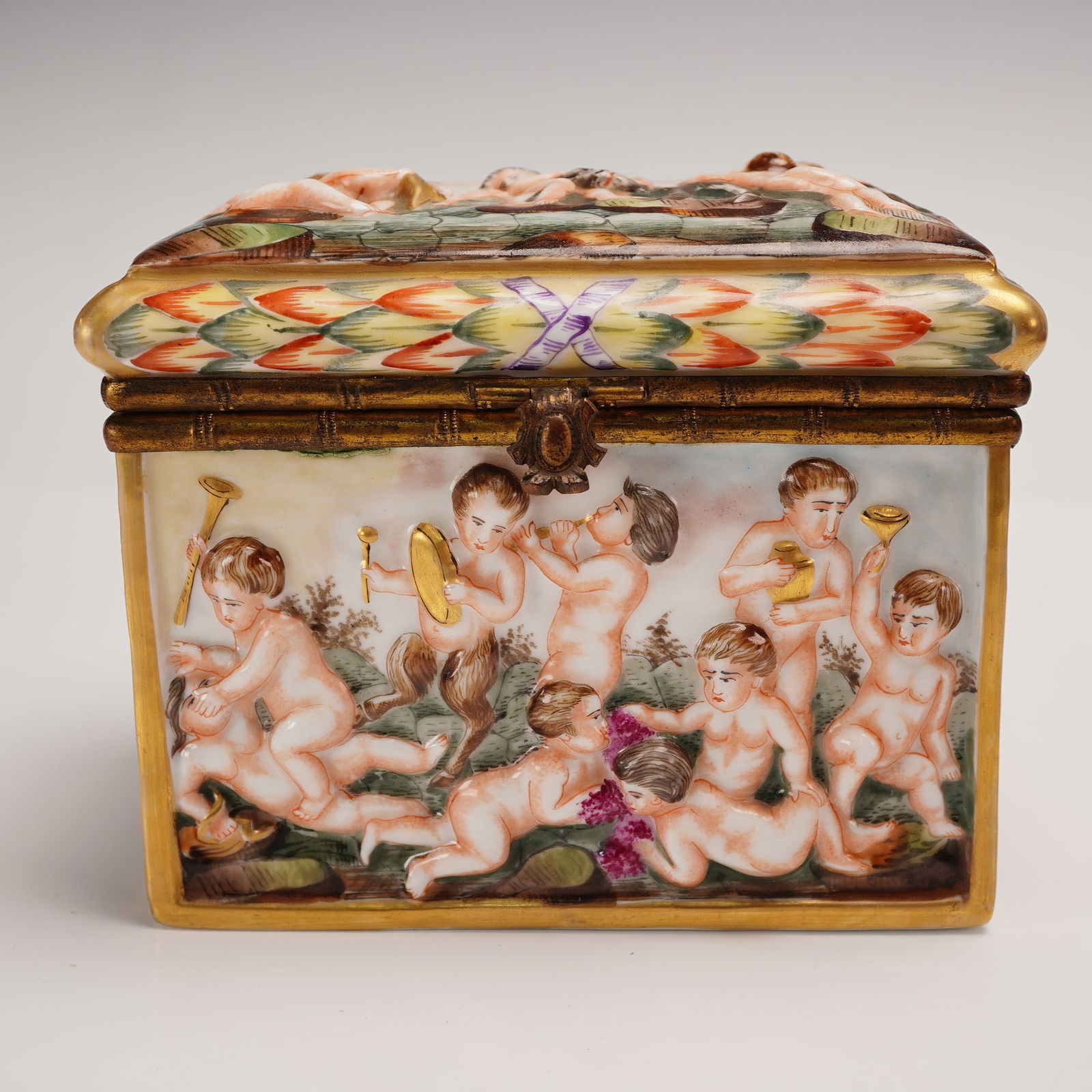 Capodimonte Porcelain Box Cherubs Playing: Charming Capodimonte-style porcelain trinket or dresser box featuring figural cherubs at play, modeled in full relief atop the domed lid. The rectangular box measures approximately 6 inches long, 4.5