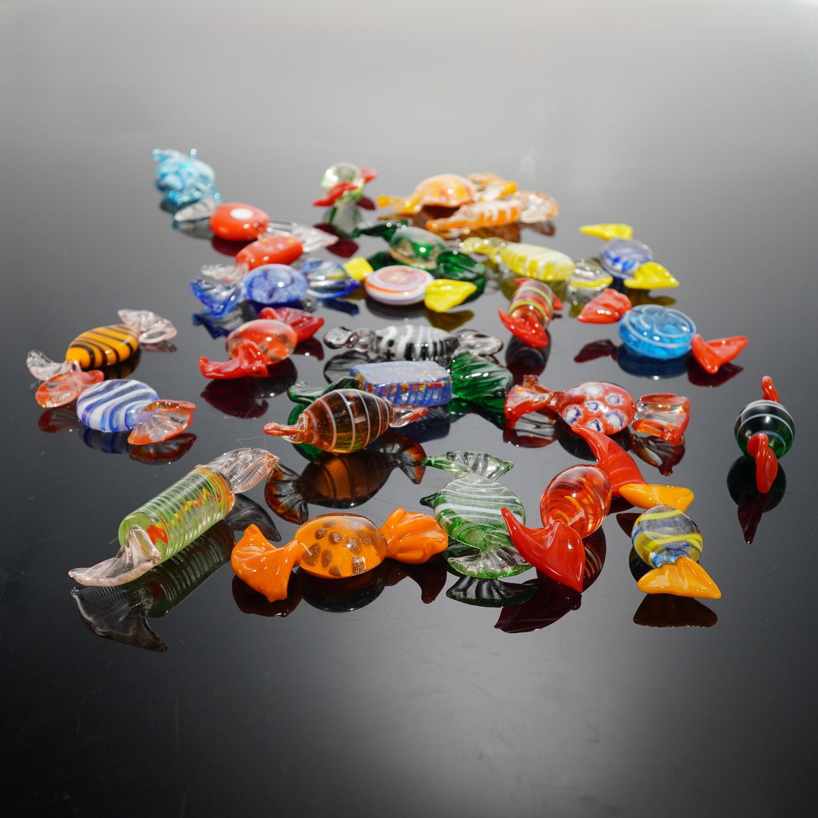 26pc Art Glass Wrapped Candy Figurines: Vibrant collection of twenty-six handblown art glass candies in assorted shapes and colors, featuring striped, swirled, and millefiori-style patterns. Each piece is crafted in clear and opaque glass w