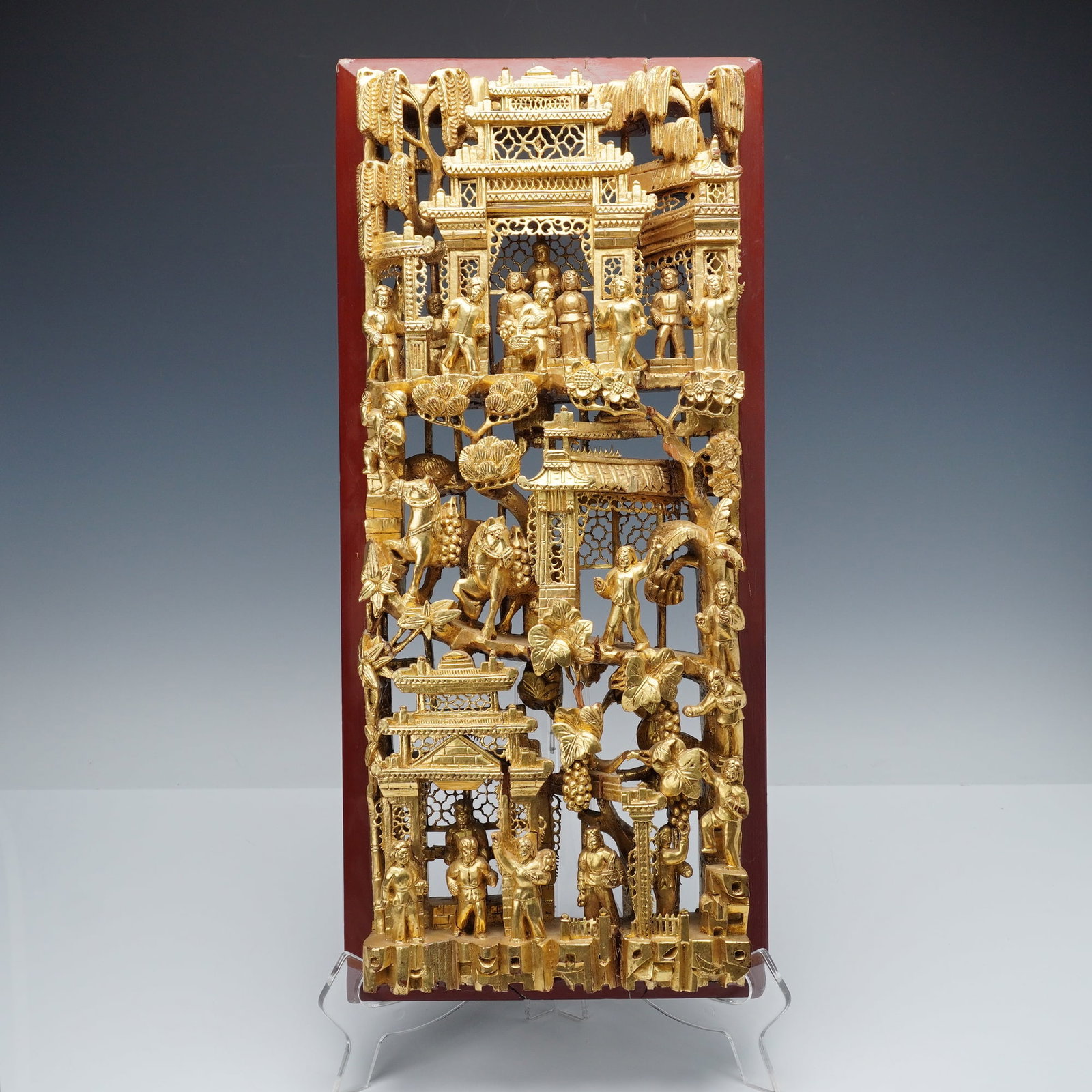 Chinese Gilt Wood Carved Market And Pavilion Scene Panel: Depicting a market and pavilion scene with numerous standing figures, attendants, and vendors above processional horses laden with goods and figures among architectural pavilions, flowering trees, and