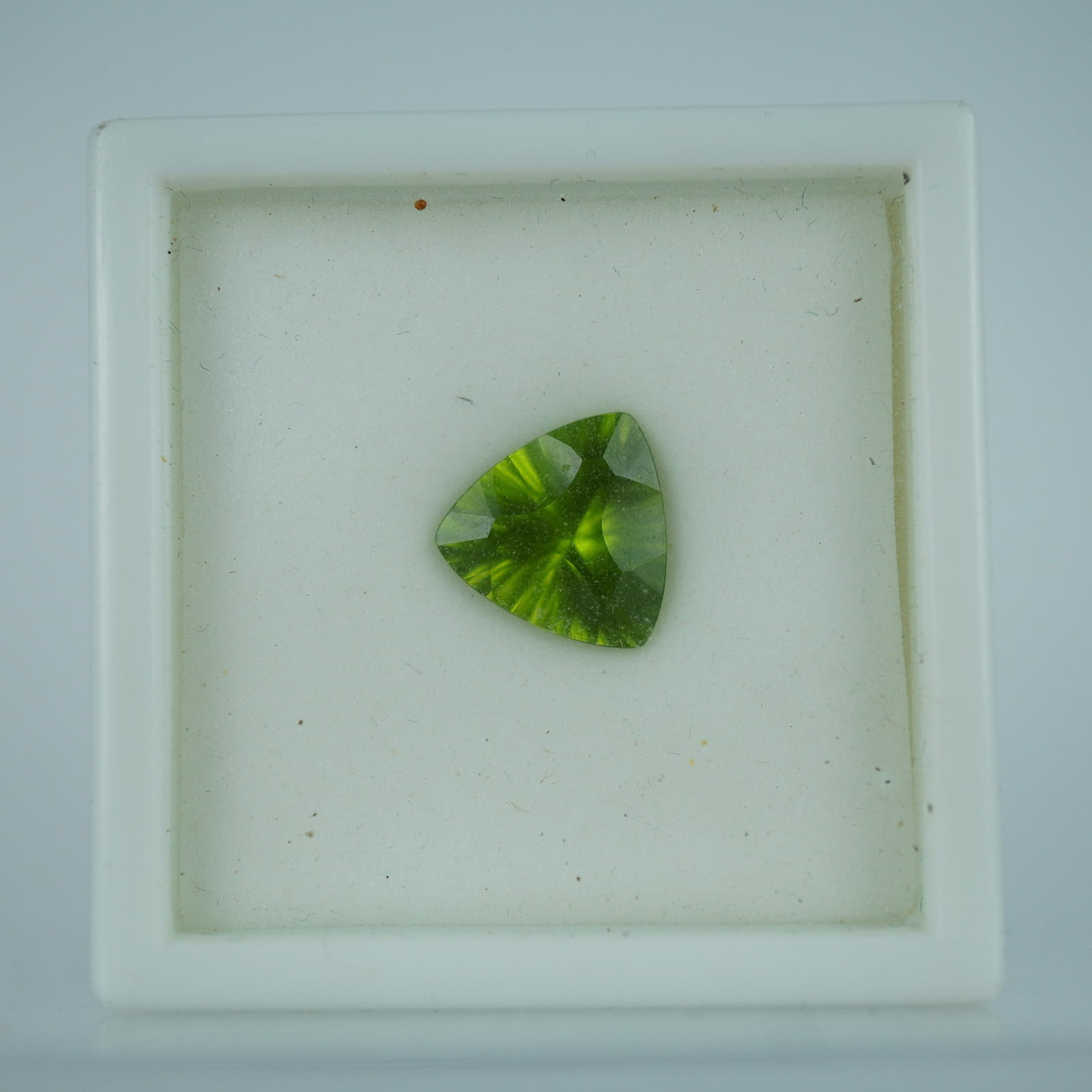 2.70 CT Peridot Trillion Cut Gemstone: Lively 2.70 carat trillion cut peridot gemstone exhibiting a rich green hue with subtle golden undertones. The stone features a precision-cut pattern that enhances its brilliance and sparkle. A vibran