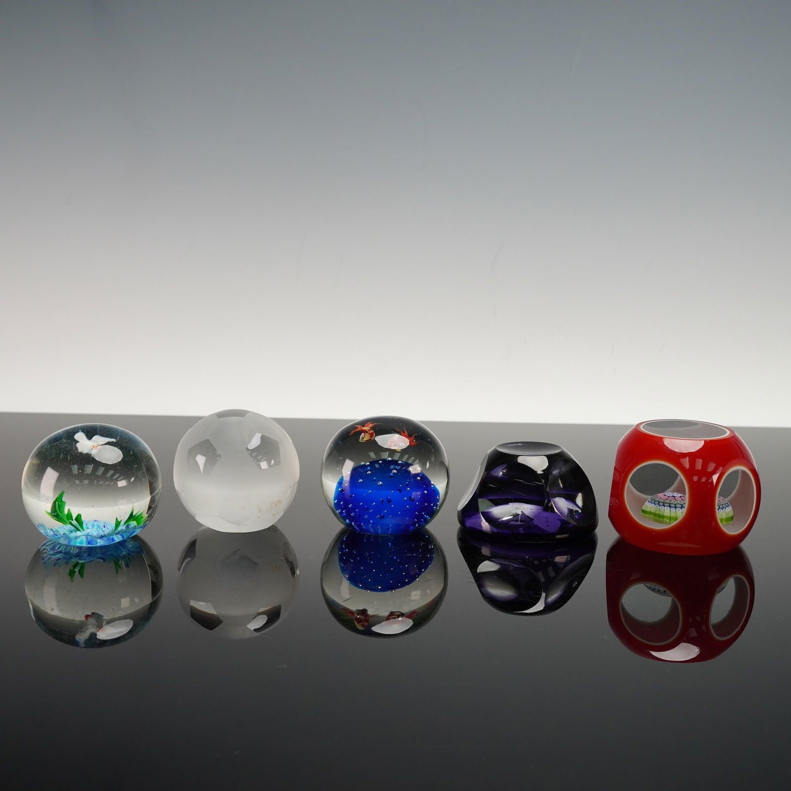 5pc Art Glass Paperweights, Including Sasaki Crystal: Group of art glass paperweights including aquarium style examples with fish and bubble decoration, a frosted faceted soccer ball, an abstract dark violet form with a butterfly, and an openwork red pap