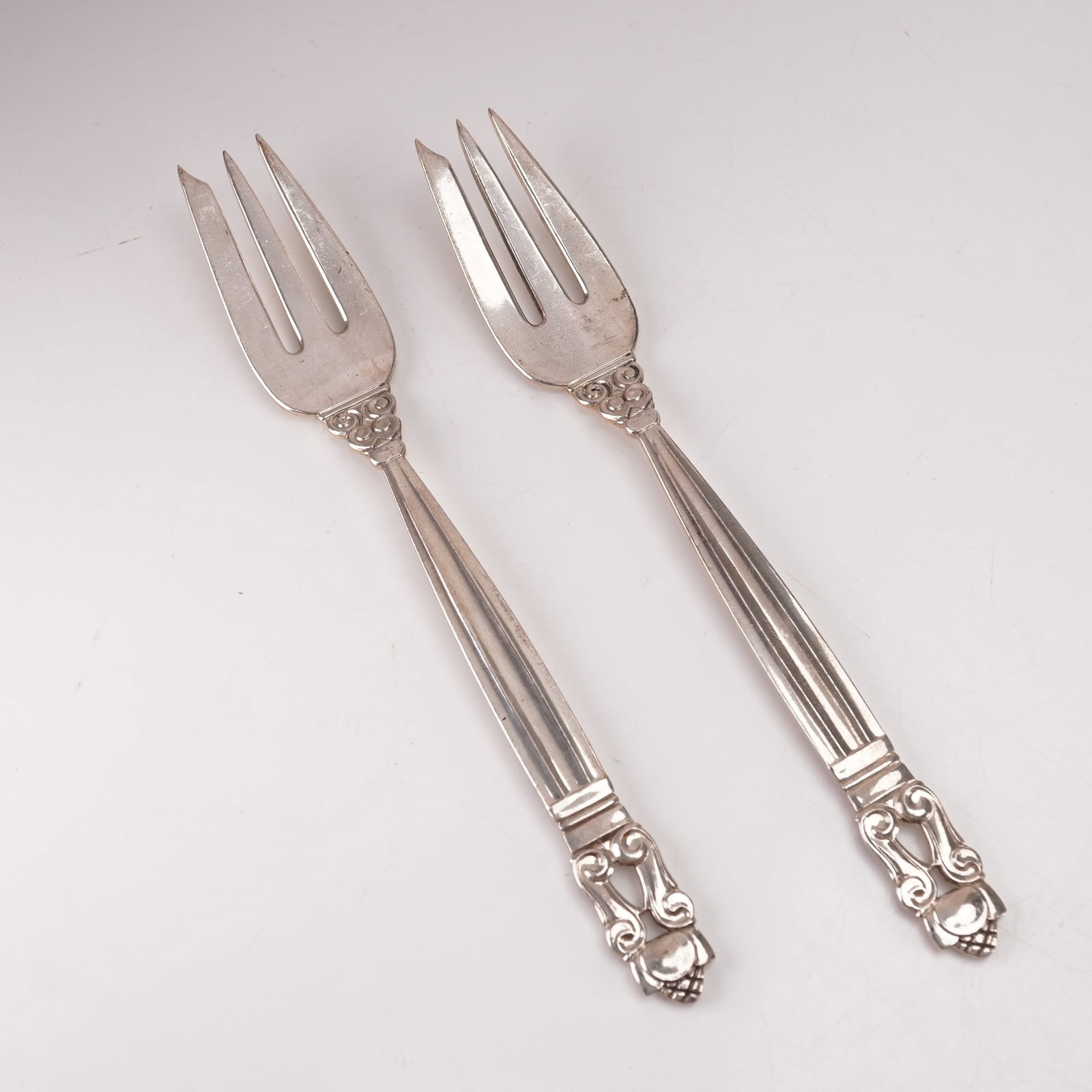 2pc Georg Jensen Sterling Silver Pastry Forks, Acorn: A two-piece lot of Georg Jensen sterling silver pastry forks in the Acorn pattern, designed by Johan Rohde in 1915. Marked Georg Jensen Sterling Denmark. The pattern features a tapered fluted handle l