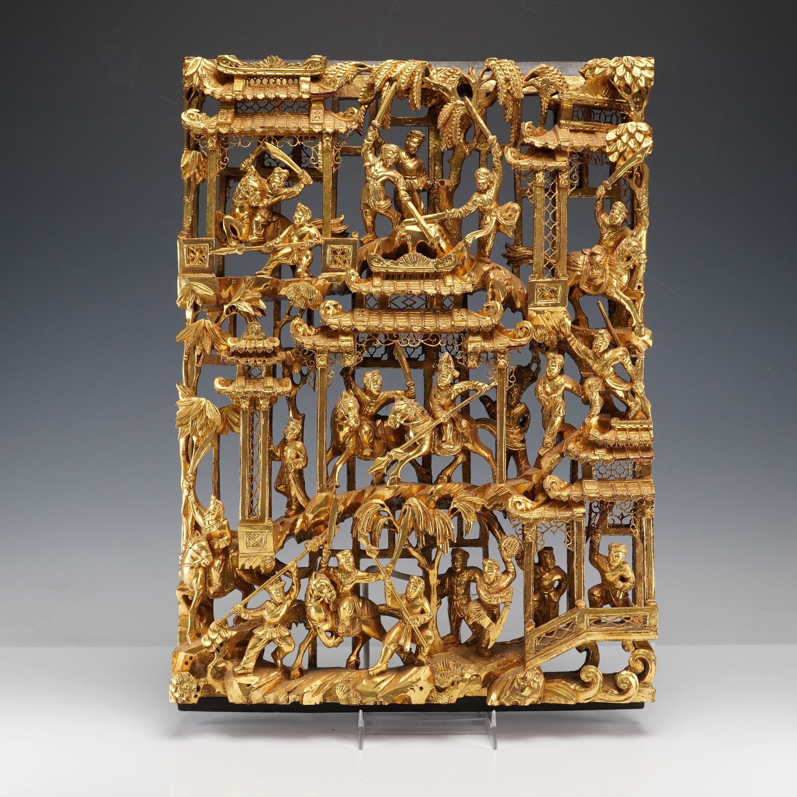 Chinese Gilt Wood Carved Battle And Pavilion Scene Panel: Depicting a battle and pavilion scene with sword wielding warriors in tiered architectural pavilions and on rocky terraces among trees and foliage, all picked out in gilt over a deeply pierced ground,