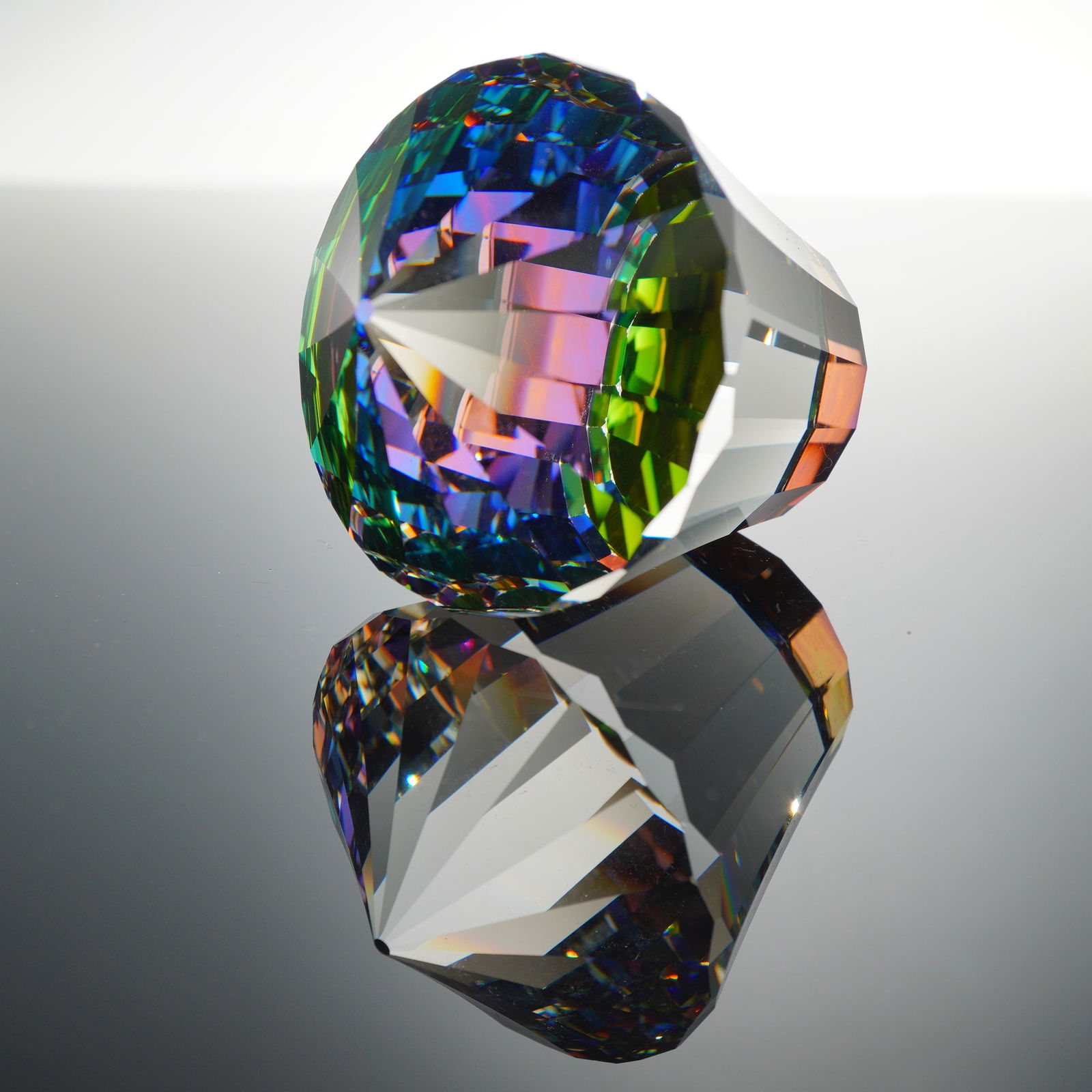 Swarovski Crystal Paperweight, Carousel: This large, faceted decorative object is crafted from crystal, cut in a modified brilliant style that tapers from a flat, felt-covered base to a pointed apex. It exhibits a prominent iridescent coatin