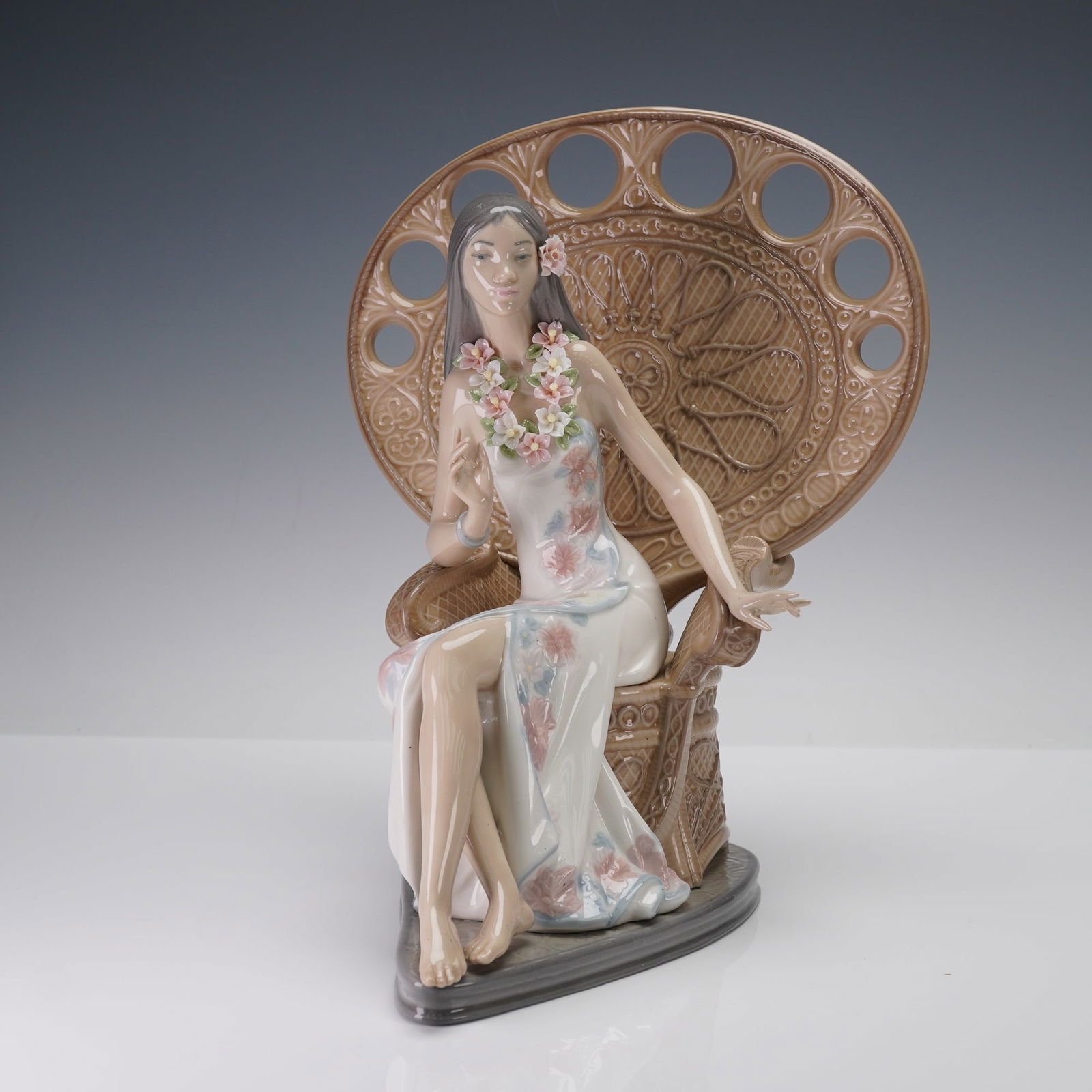 Lladro Porcelain Figurine, Hawaiian Beauty 01001512: Figurine of an elegant island woman seated gracefully in an intricately modeled wicker peacock chair. Wearing a flowing floral dress in soft pastels and adorned with a delicate hand-applied flower lei