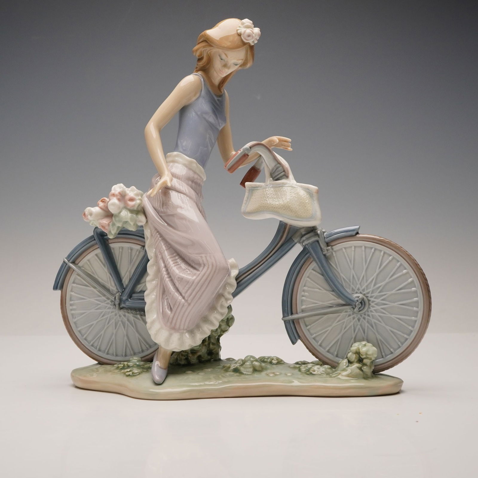 Lladro Porcelain Figurine, Biking in the Country 1005272: This glazed porcelain piece depicts a young woman with a flower in her hair, dressed in a lavender top and a pink and white striped ruffled skirt. The bicycle features a front basket and a bouquet of