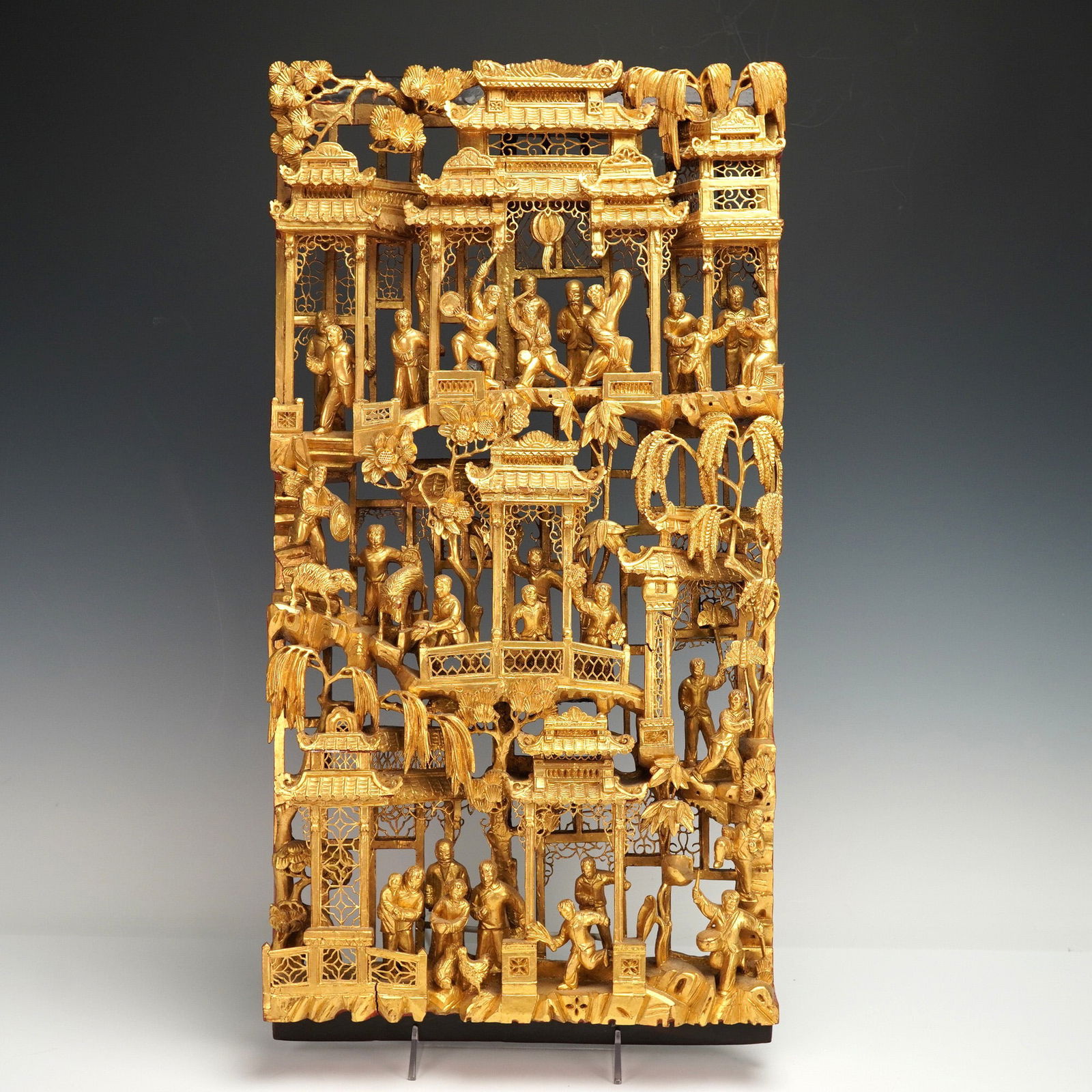 Chinese Gilt Wood Carved Celebration Scene Panel: Depicting a lively celebration and pavilion scene with numerous standing and dancing figures on terraces and bridges among architectural pavilions, and trees, all picked out in gilt over a deeply pier