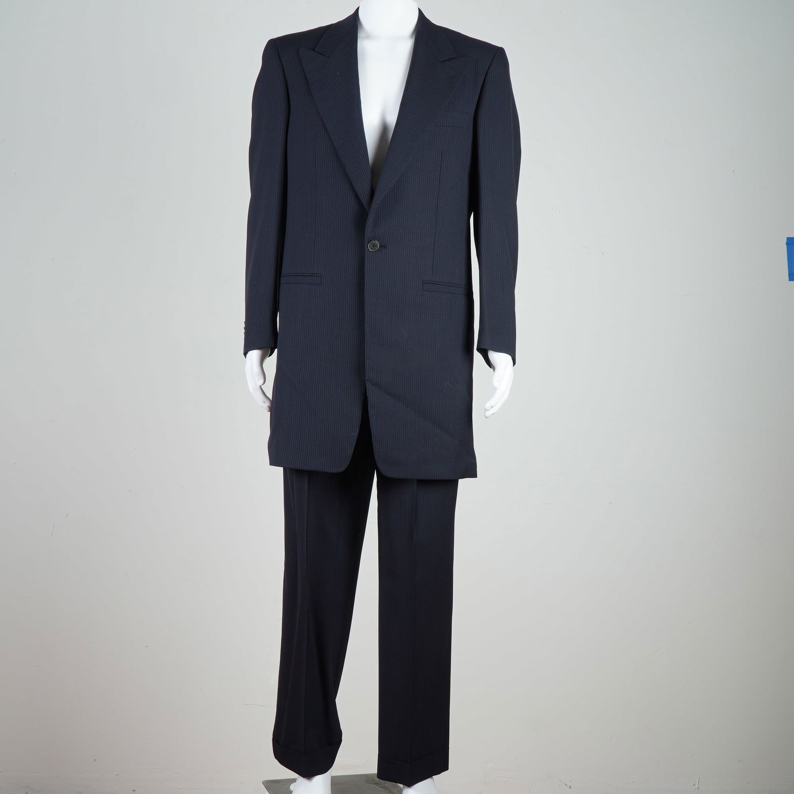 Gianni Versace Navy Pinstripe Suit: This navy pinstripe suit presents a precisely tailored silhouette comprising a structured single-breasted jacket paired with matching trousers, both designed in a fine striped textile. The jacket feat