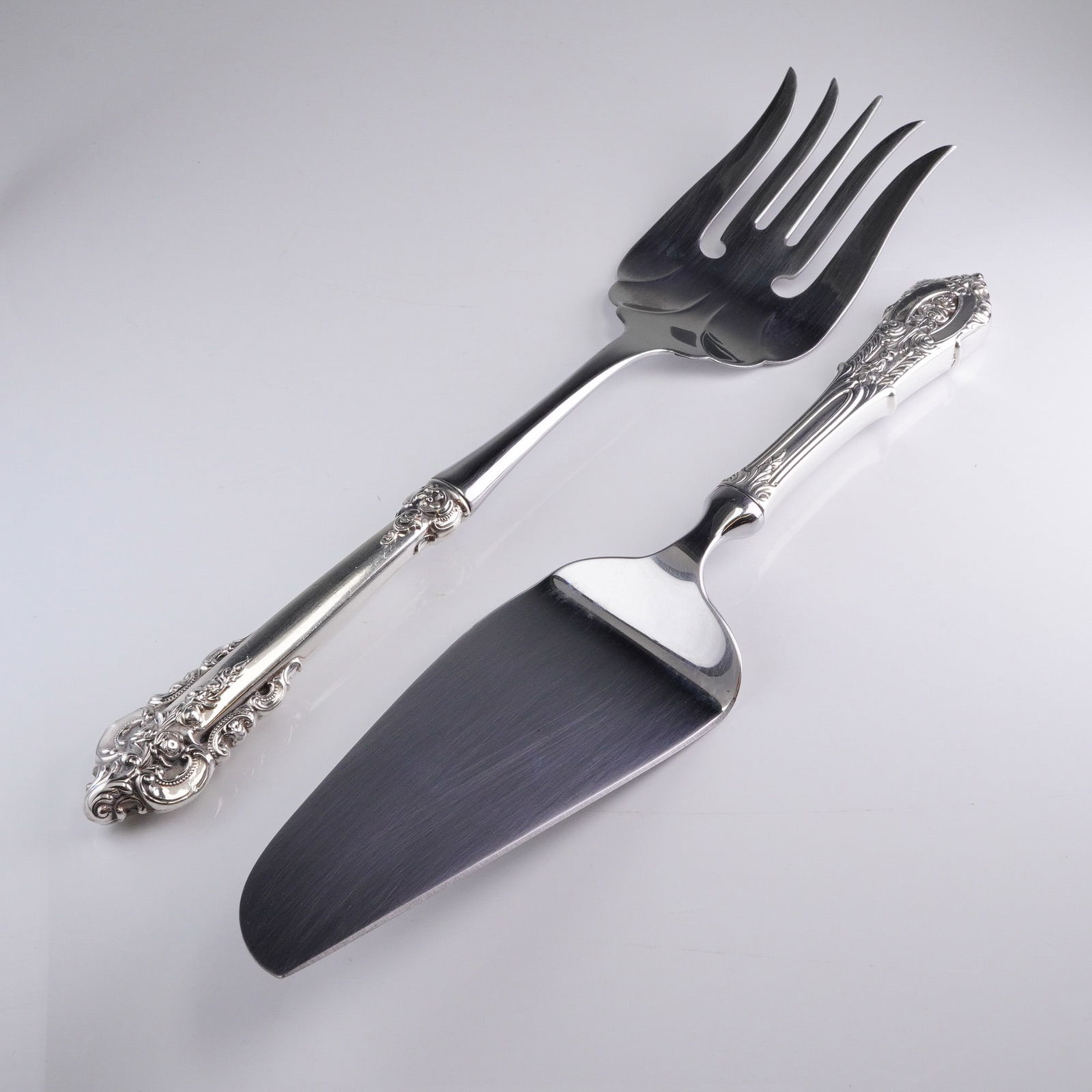 A Pair of Wallace Grande Baroque Sterling Handle Serving Utensils: A pair of serving utensils by Wallace Silversmiths in the highly detailed Grande Baroque pattern. This 2pc. lot includes one large four-tine serving fork and one cake or pie server. Each piece feature