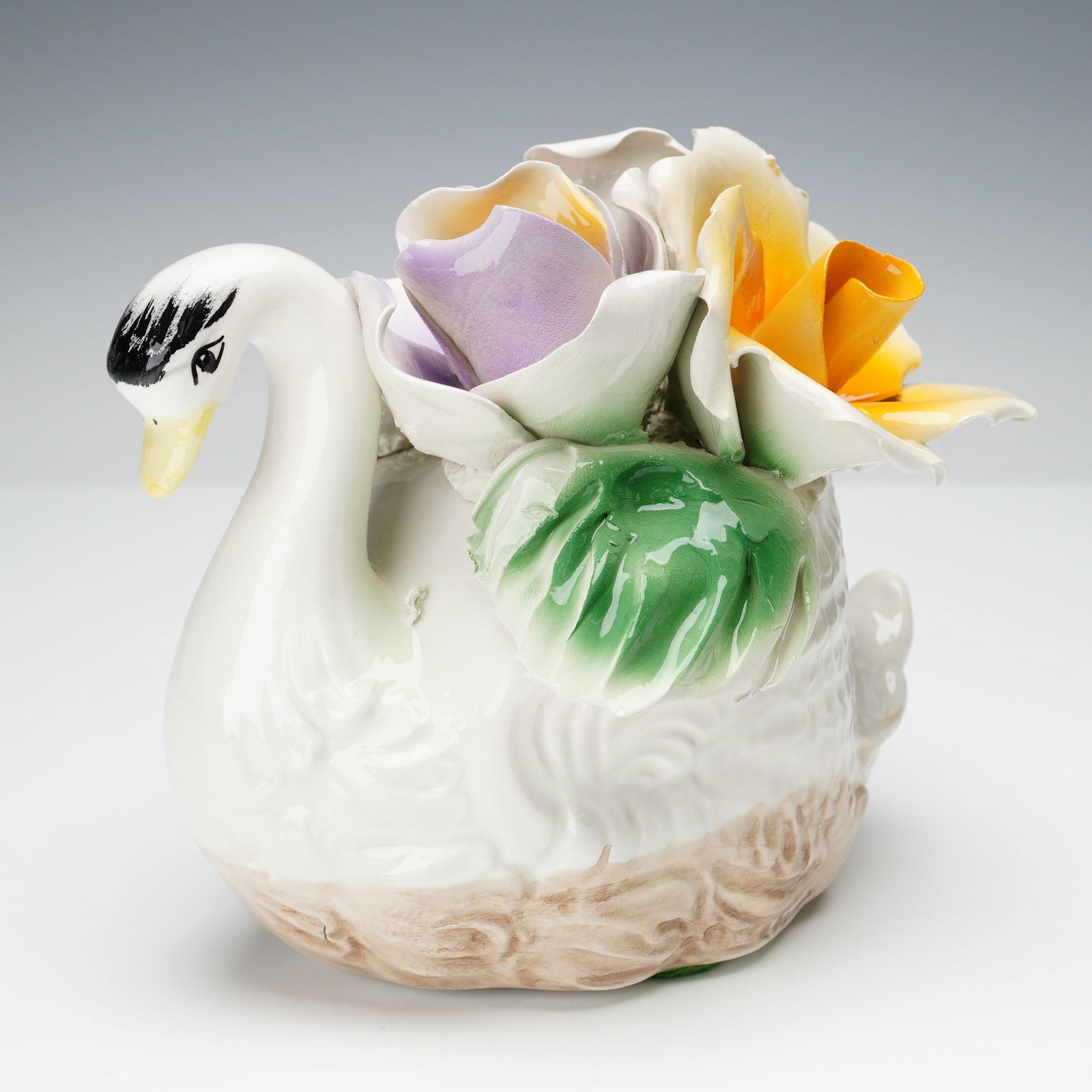 Capodimonte Porcelain Swan with Flowers: Capodimonte porcelain figurine of a swan adorned with hand-crafted flower blossoms in pastel shades of purple, yellow, and white with green leaves. Detailed sculpting and high-gloss glaze typical of C