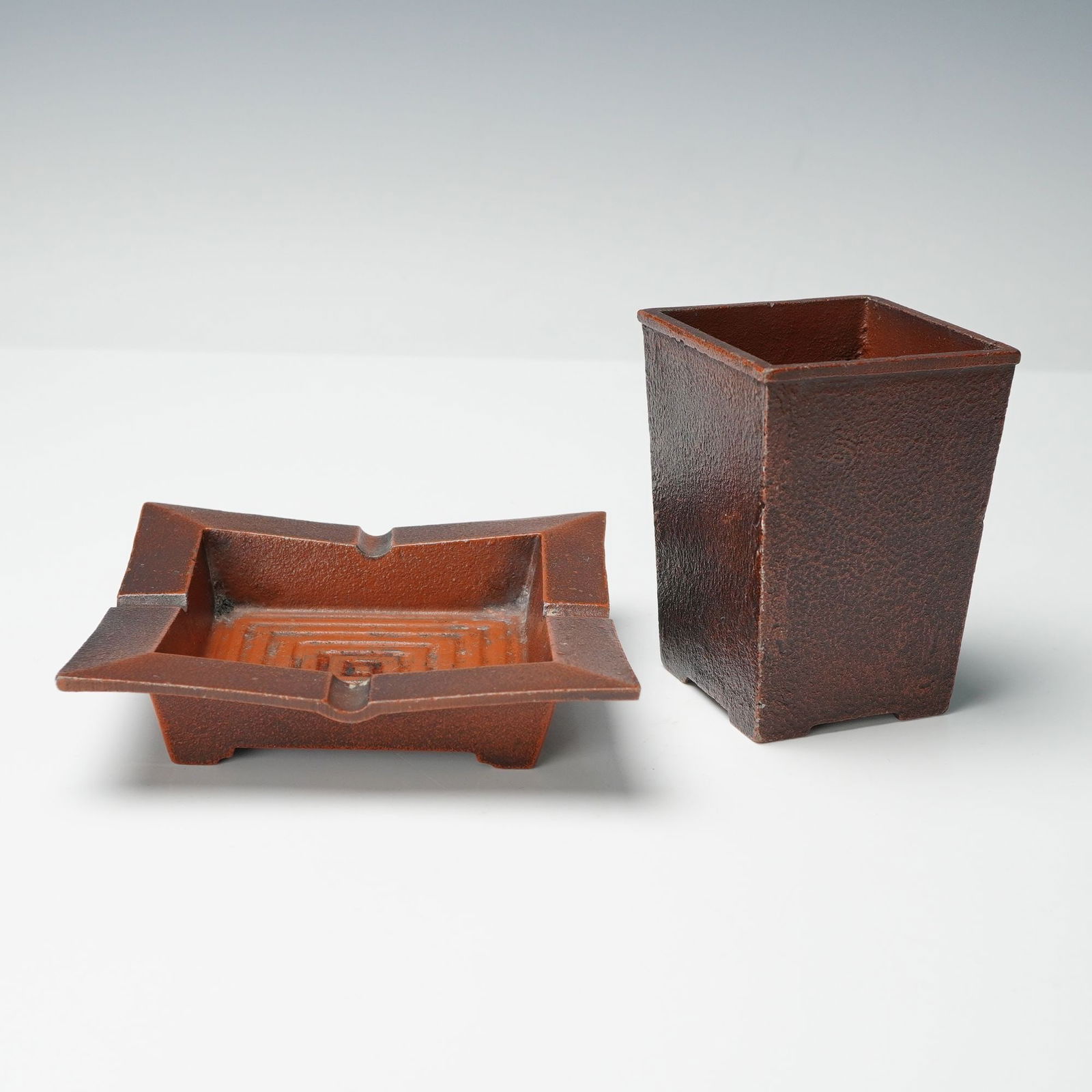2pc Cast Iron Ashtray and Pencil Box Set: Pair of cast iron desk accessories in a mid century modern style with geometric lines and a rich rust brown finish. The set includes a square ashtray with stepped interior design and a matching tapere