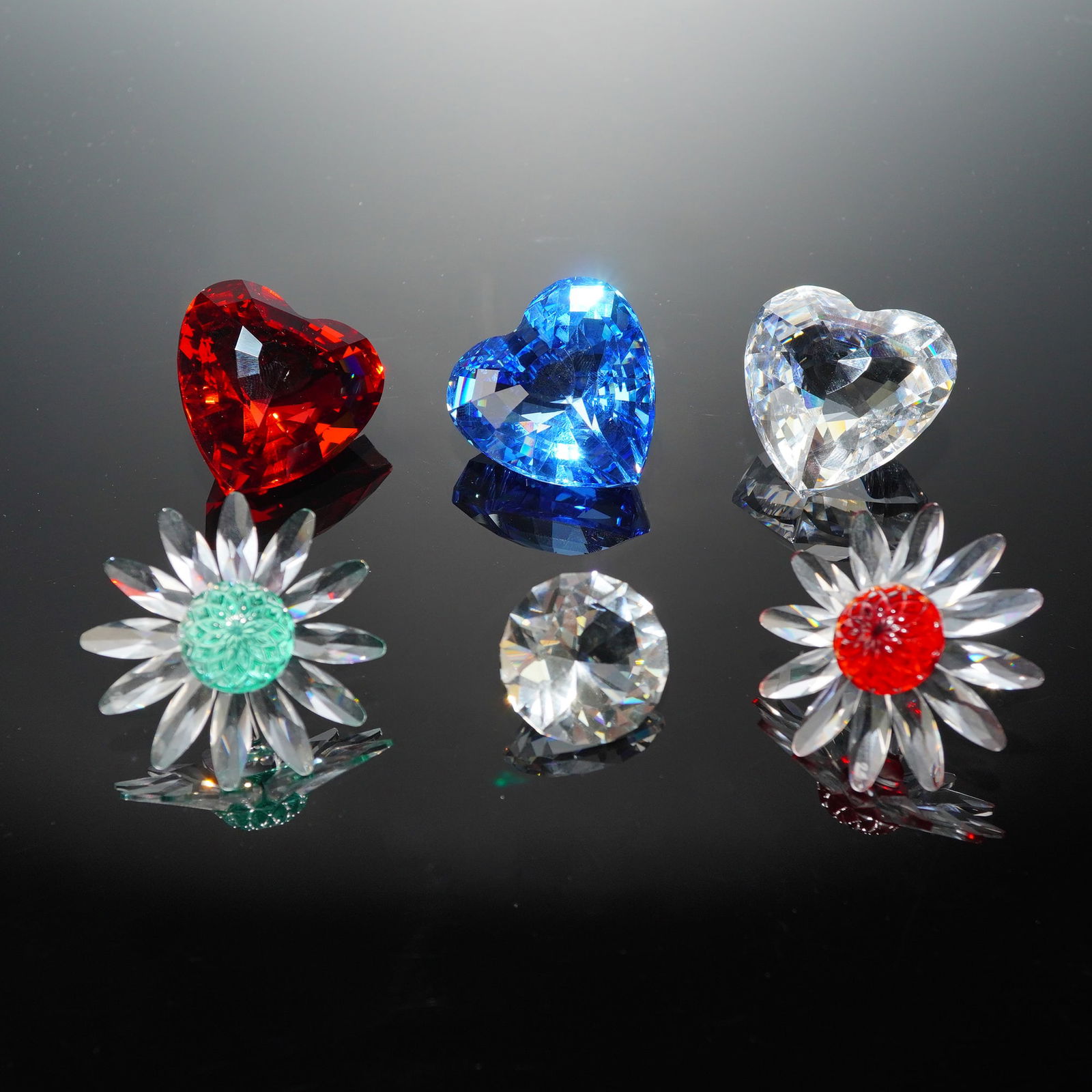 6pc Swarovski Crystal Decorative Objects and Paperweights: Six individual Swarovski crystal decorative objects. The primary components feature heavily faceted hearts in ruby red, sapphire blue, and clear crystal. The hearts bear the etched Swarovski swan logo
