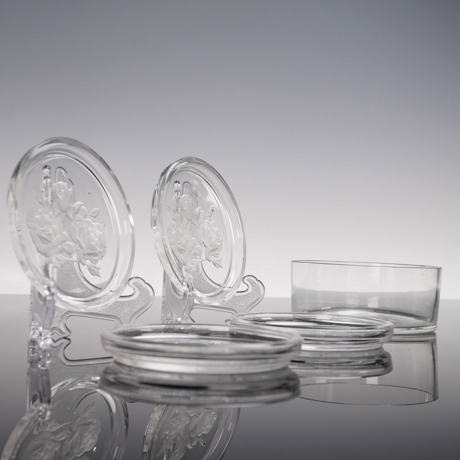 5pc Etched Crystal Rose Coasters with Holder: Set of five etched crystal coasters featuring a detailed rose motif in frosted relief, accompanied by a matching crystal holder. The coasters display fine craftsmanship with elegant floral decoration,