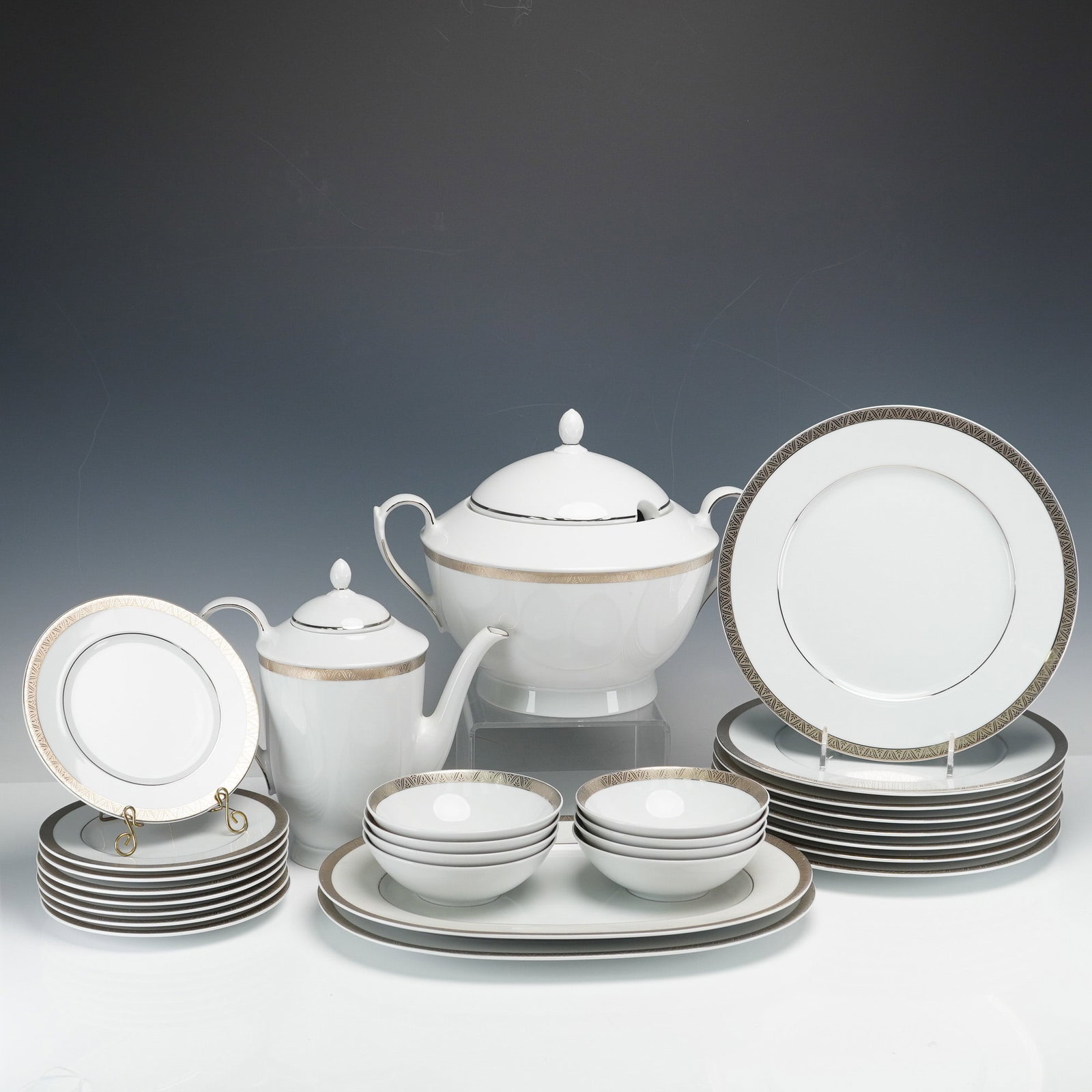 A Collection of 28 Pieces of Falken-Porzellan Bavaria Gilt Dinnerware: A collection of thirty pieces of white porcelain dinner and serving ware manufactured by Falken Porzellan, Bavaria, Germany. The service is executed in a clean, modern style featuring gilt decoration.