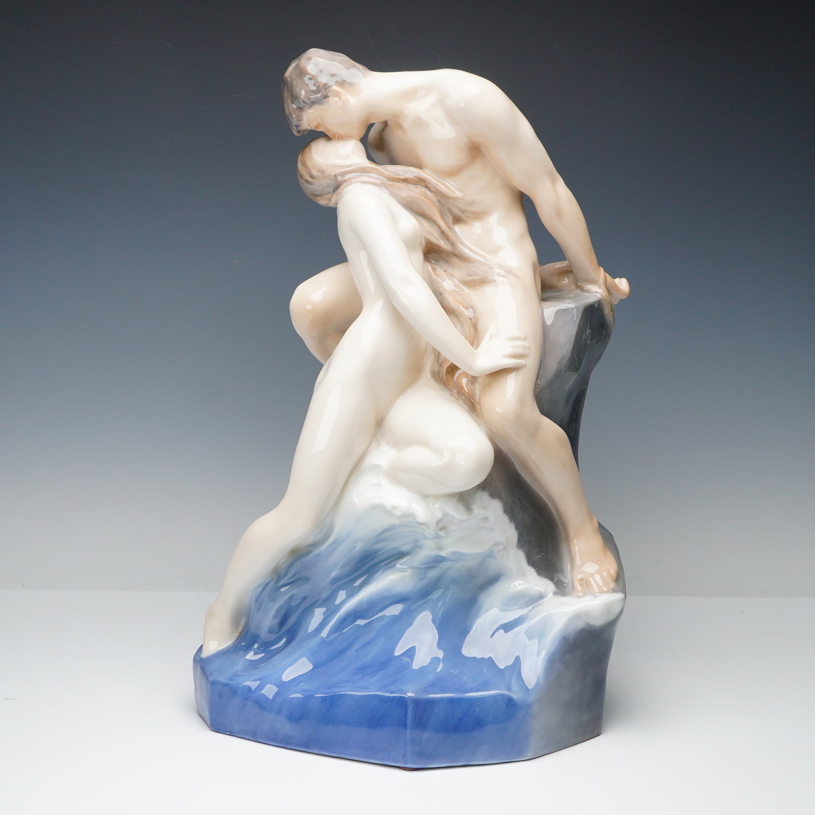 Royal Copenhagen Porcelain Sculpture, The Wave and the Rock: Presented here is a Royal Copenhagen porcelain sculpture modeled as a nude couple embracing on a rocky outcrop with waves rising behind them, based on an 1897 design by Swedish sculptor Johan Theodor
