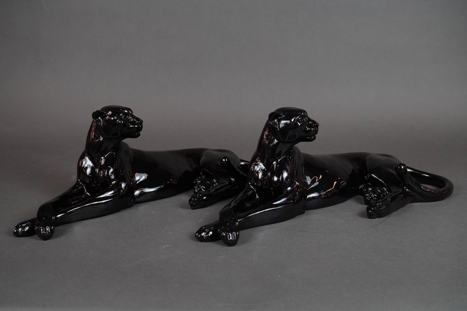 A Pair of Art Deco Style Black Glaze Panther Figurines: A pair of stylized decorative figures, depicting two panthers resting in a prone position. The sleek, streamlined form is characteristic of the Art Deco period. The figures are constructed from a mold