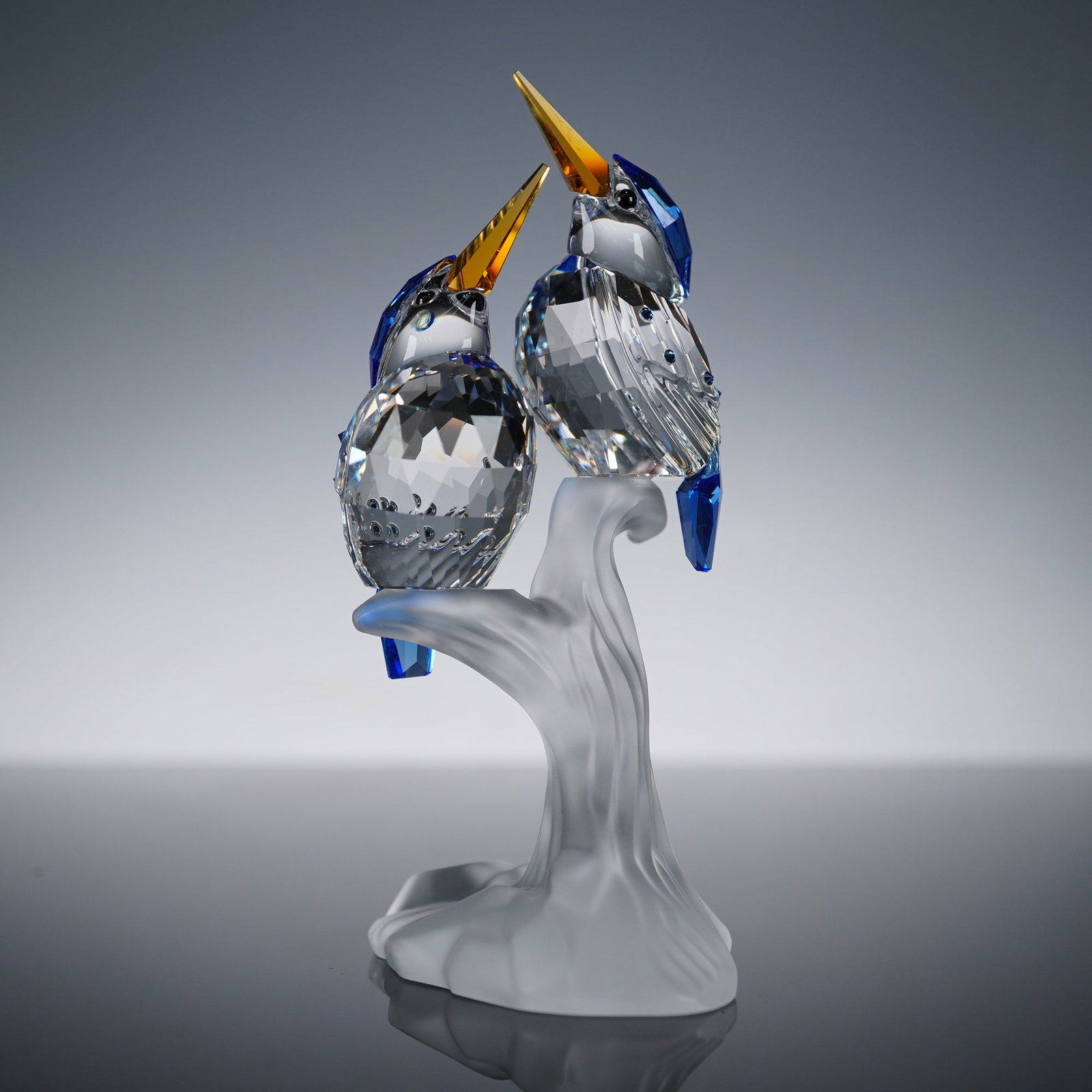 Swarovski Crystal Figurine Malachite Kingfishers: A single crystal figurine manufactured by Swarovski, 'Malachite Kingfishers' model. The sculpture depicts a pair of highly stylized kingfishers perched on a frosted crystal branch support. The piece i