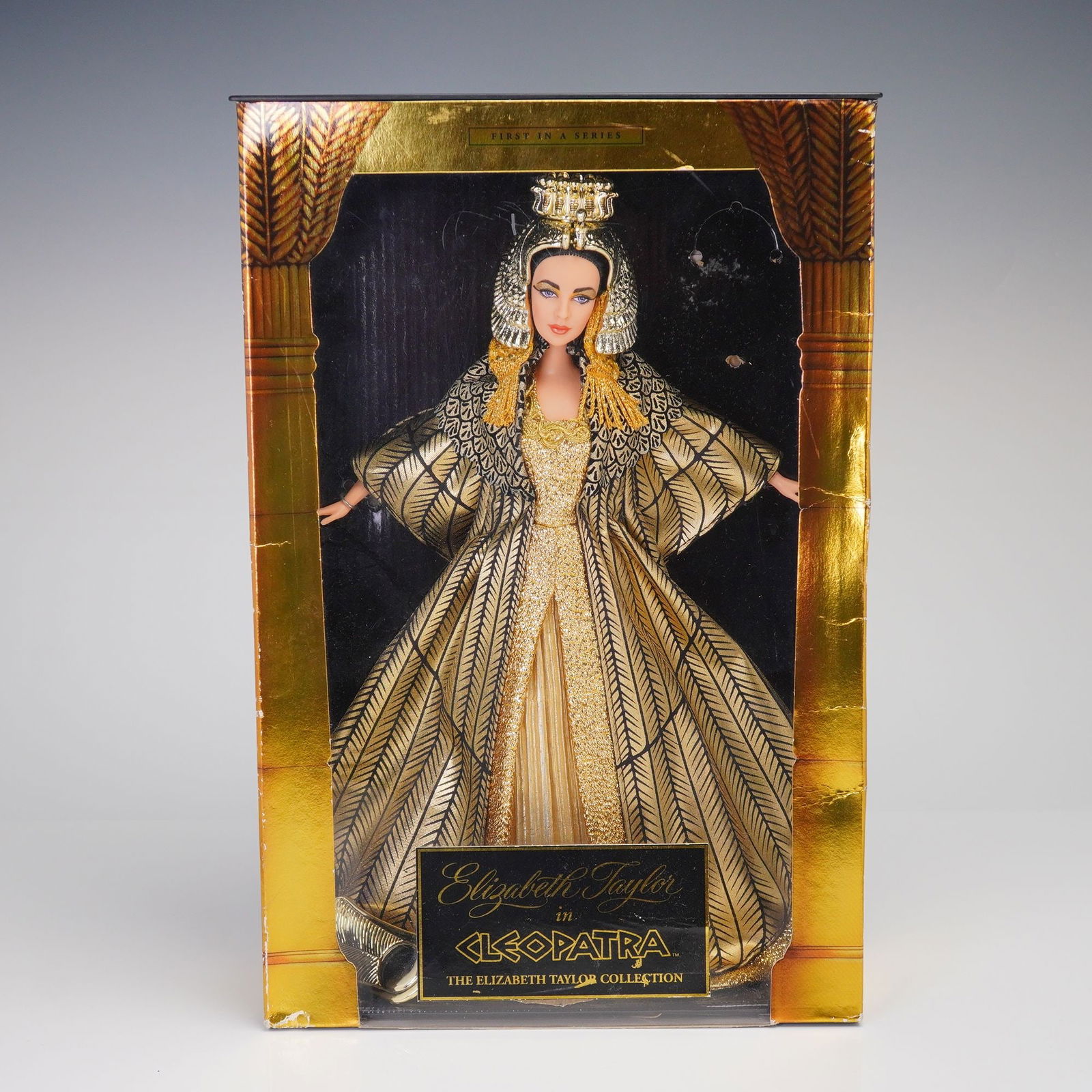 Mattel Elizabeth Taylor in Cleopatra Barbie Doll 1999: A collectible fashion doll produced by Mattel in 1999, depicting actress Elizabeth Taylor in her role as Cleopatra. This item is identified as Model D0266 and is marked "FIRST IN A SERIES" within "THE